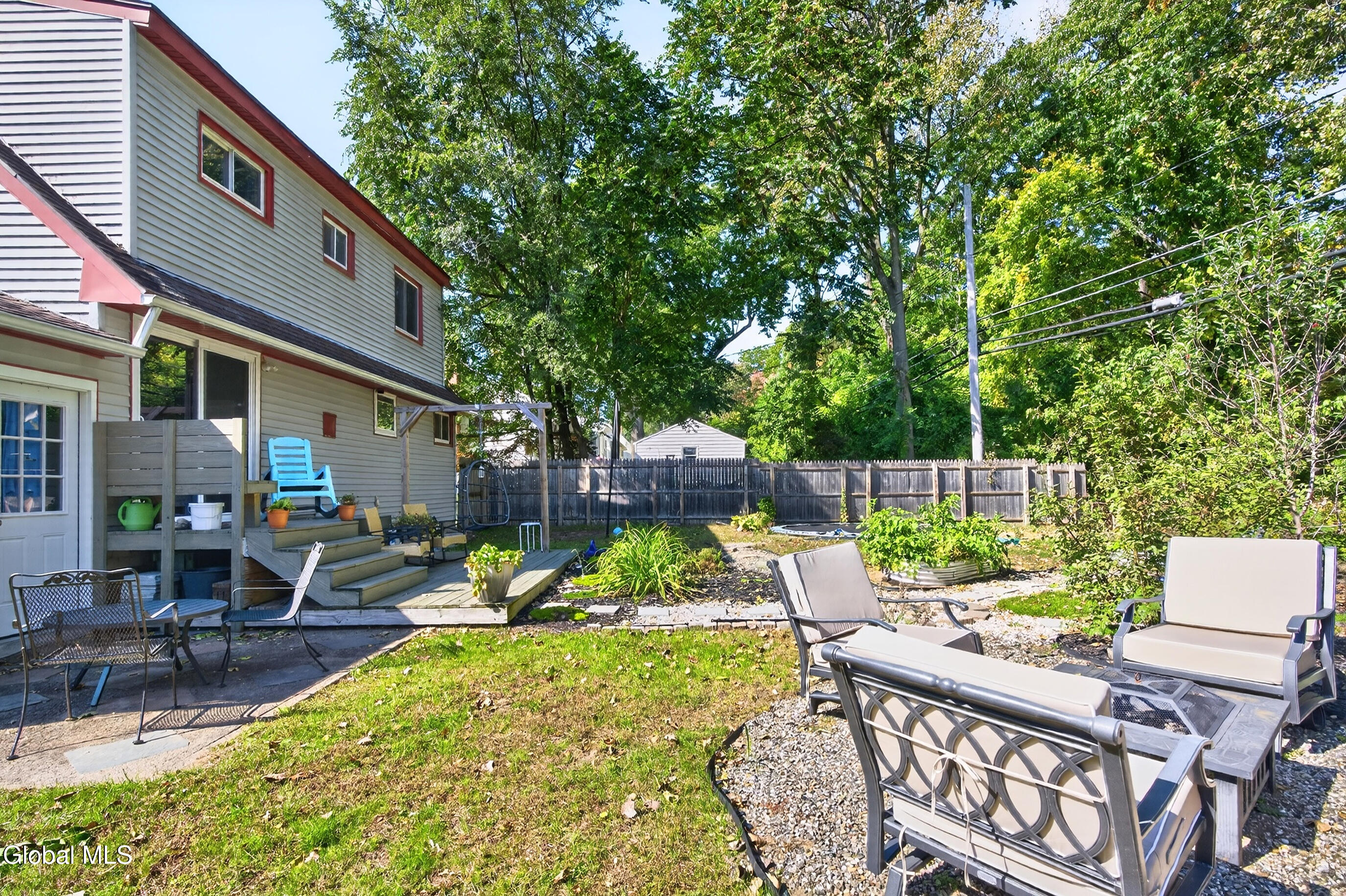 Backyard patio with raised deck, outdoor seating, garden beds, and mature trees beside the house.