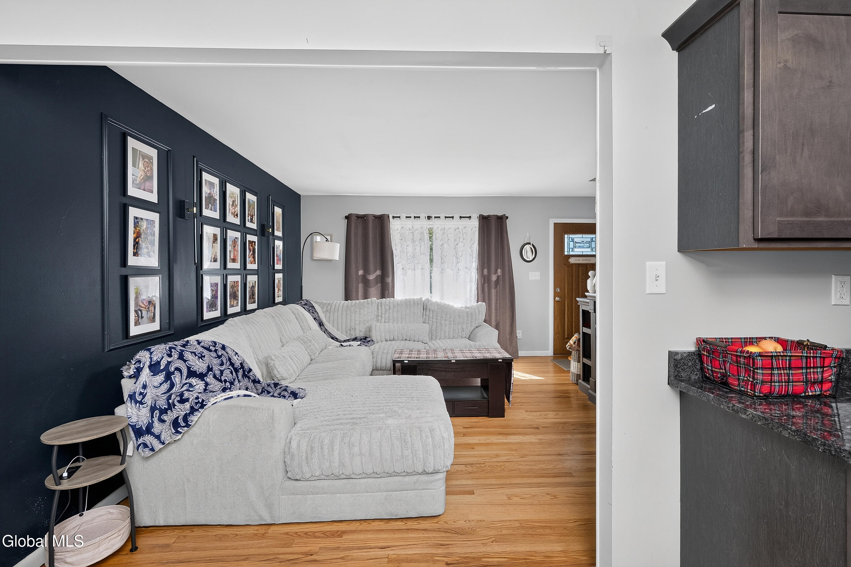 Living room with a white sectional, gallery wall on a dark accent wall, and hardwood floors.