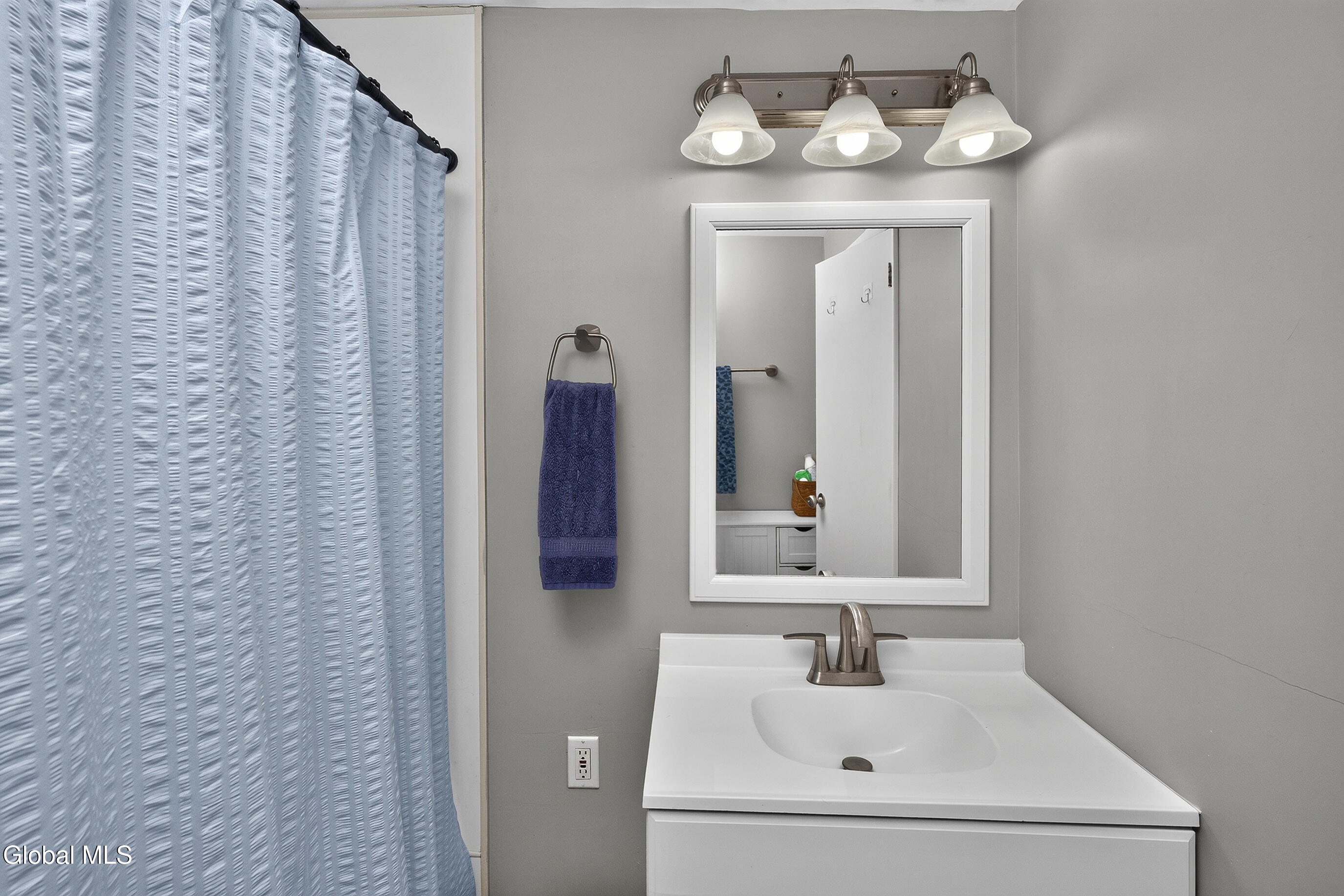 Bathroom vanity with framed mirror and three-light fixture beside a blue shower curtain.