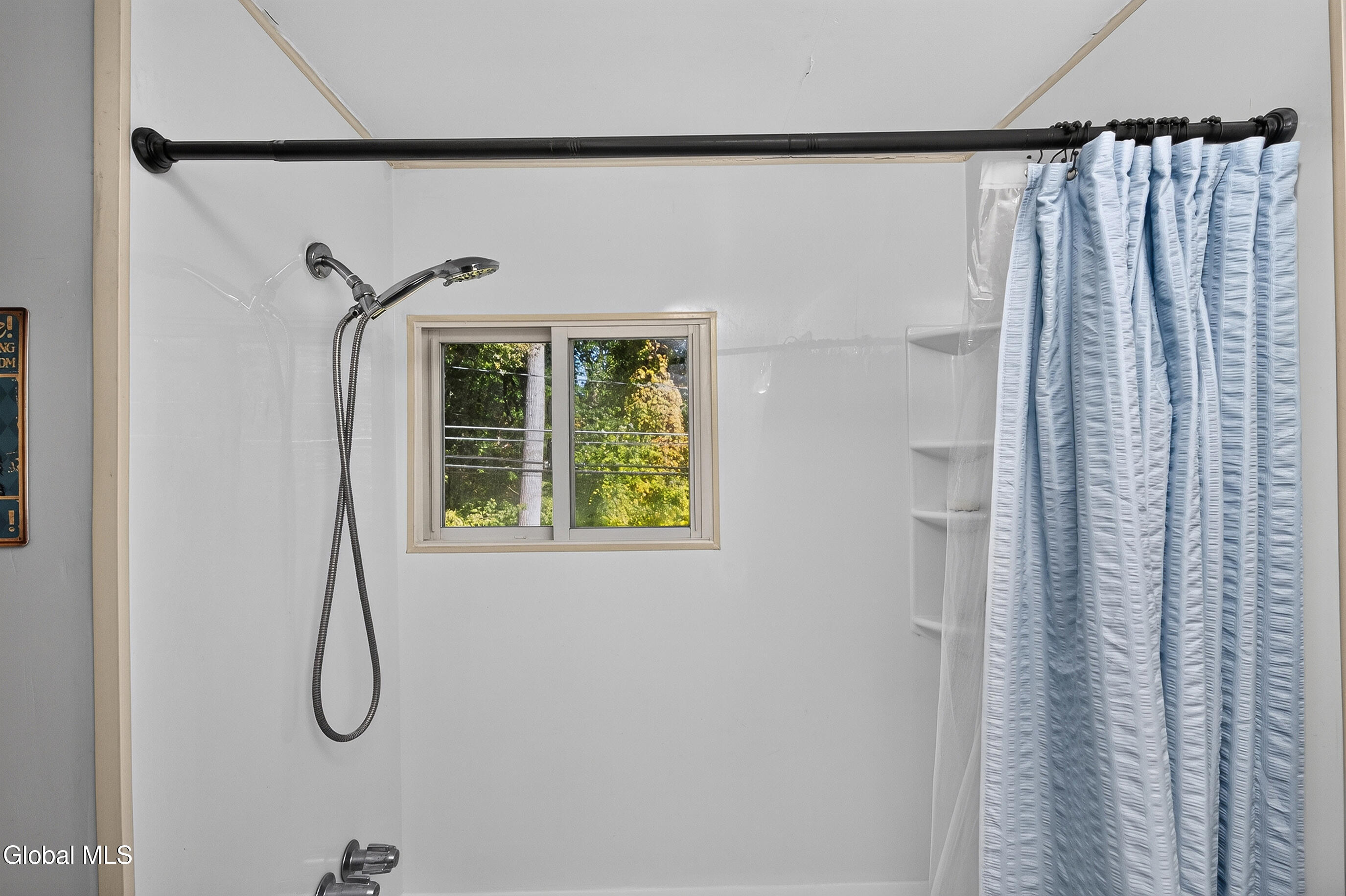 White-tiled shower with a window, handheld showerhead, built-in shelves, and light blue curtain.