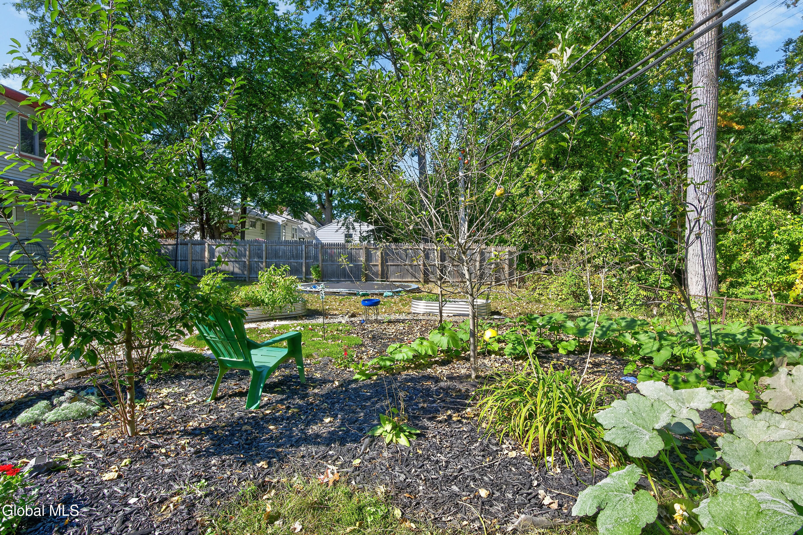 Leafy backyard garden with a green Adirondack chair, raised beds, and a small above-ground pool.