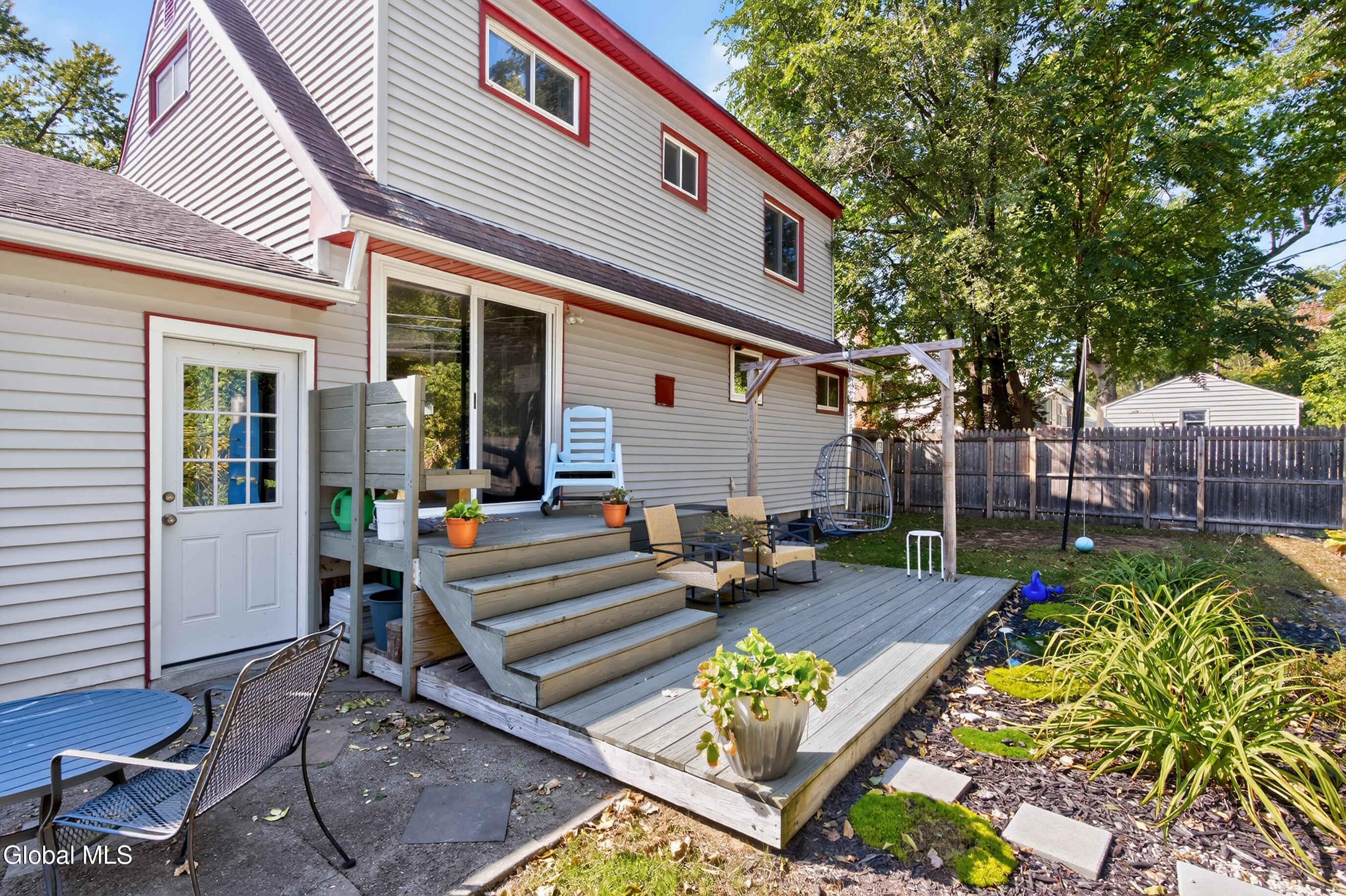 Rear of a two-story house with a raised deck, broad steps, patio seating, and a pergola.