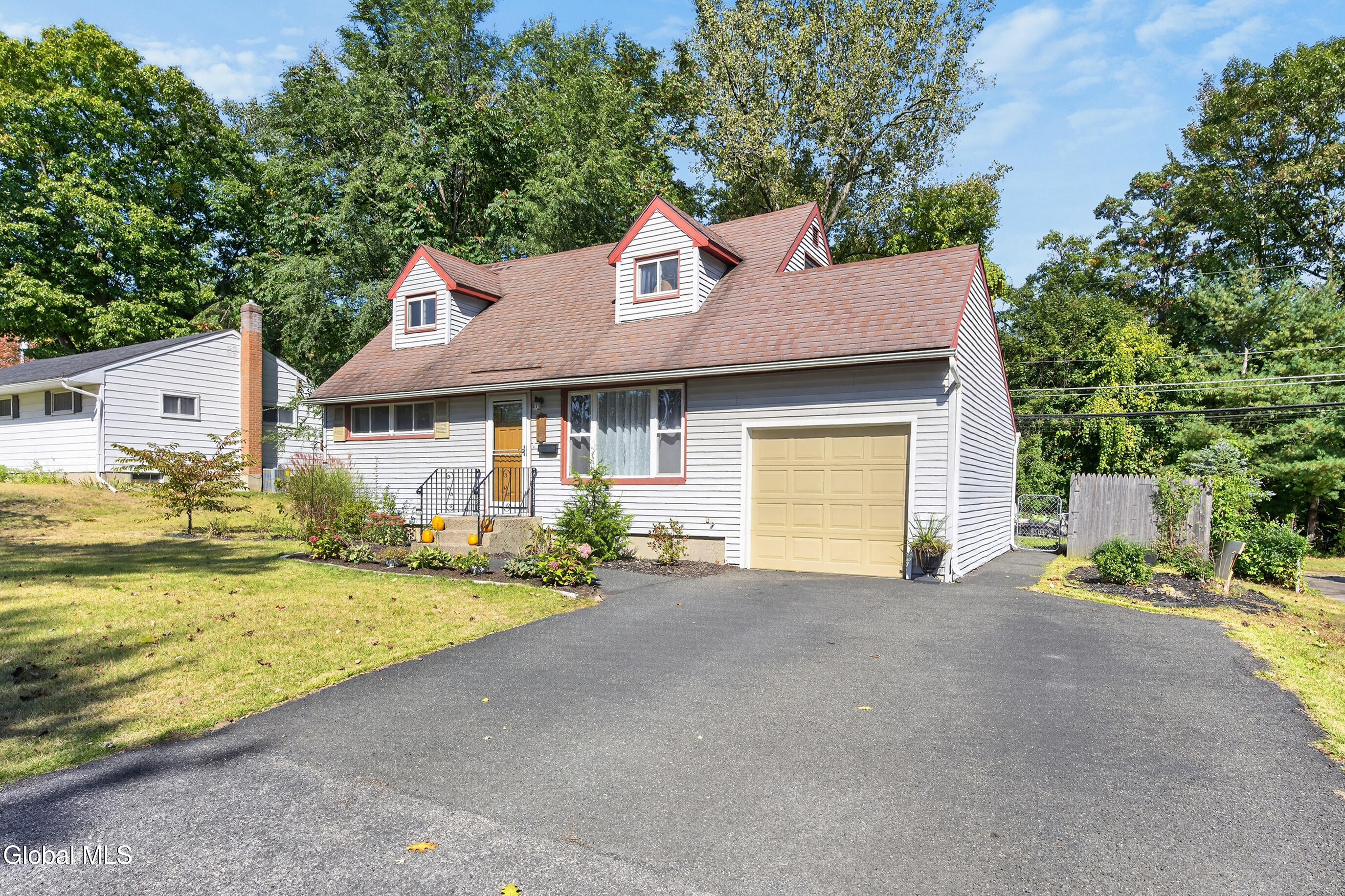 White-sided house with red-trimmed dormers, yellow garage door, and broad driveway.