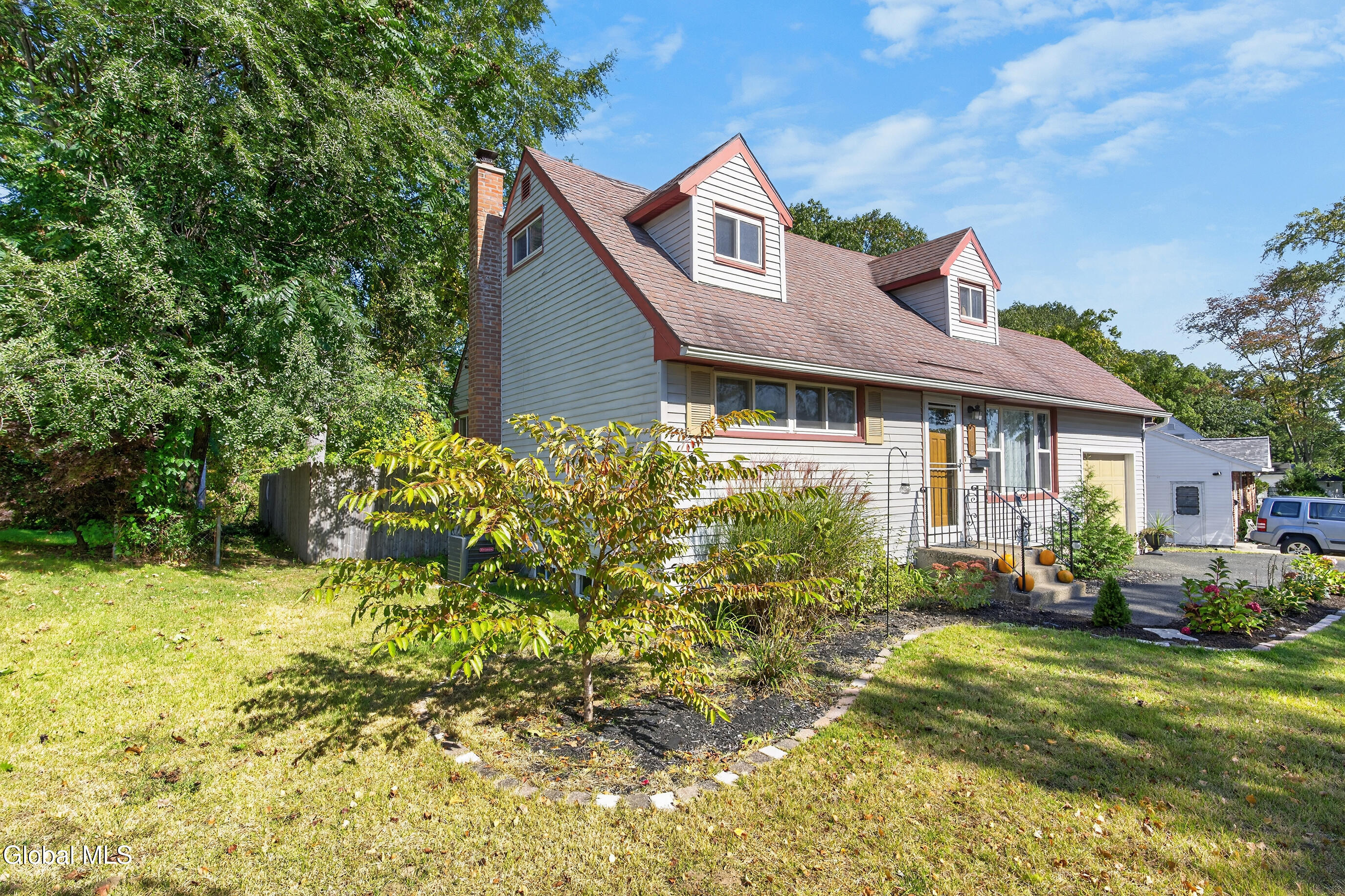 House with red-trimmed dormers, a brick chimney, attached garage, and landscaped front garden.