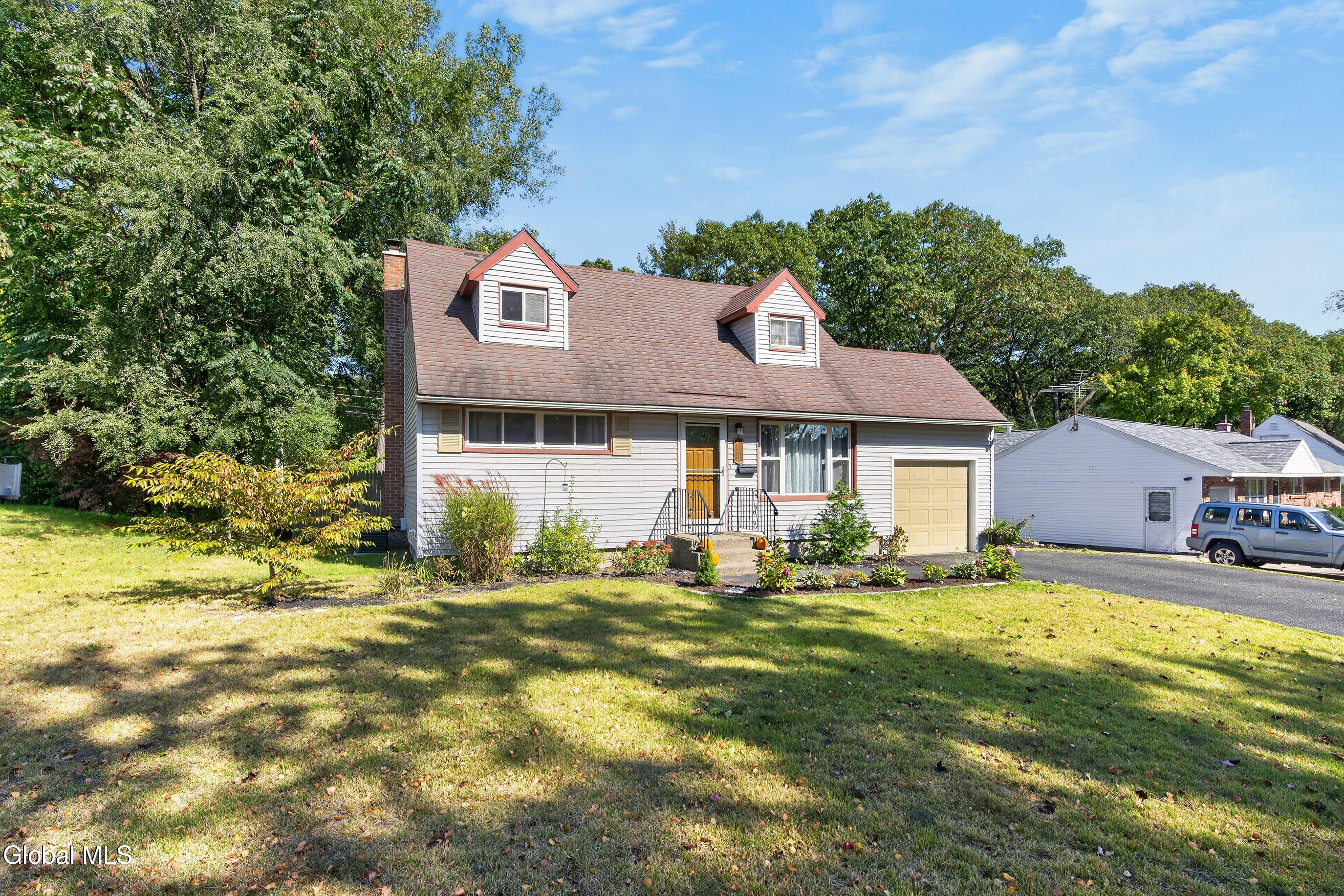 House with red-trimmed dormers, yellow front door, attached garage, and landscaped front lawn.