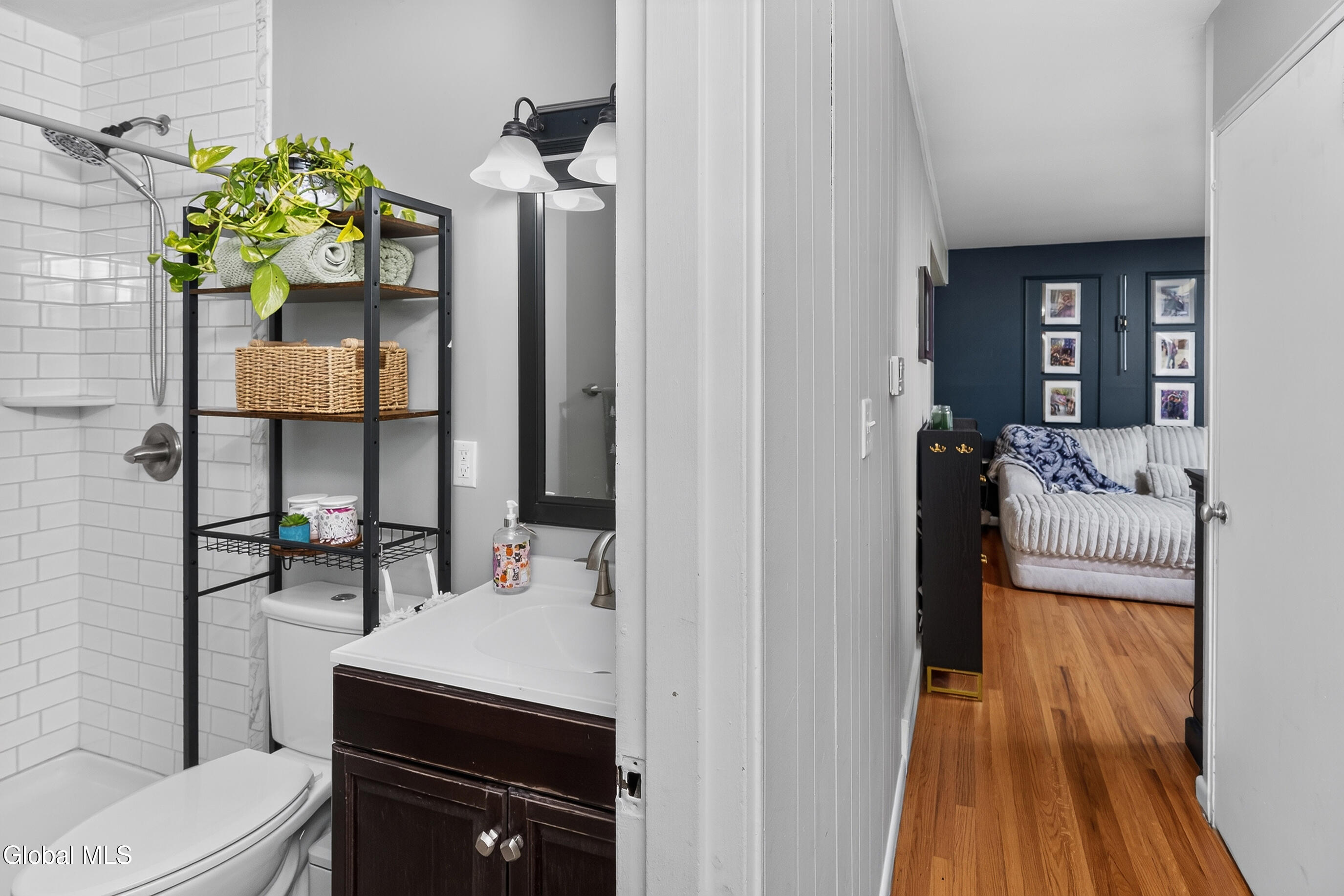 Bathroom with white subway-tile shower and dark vanity, opening onto a hallway and furnished living room.