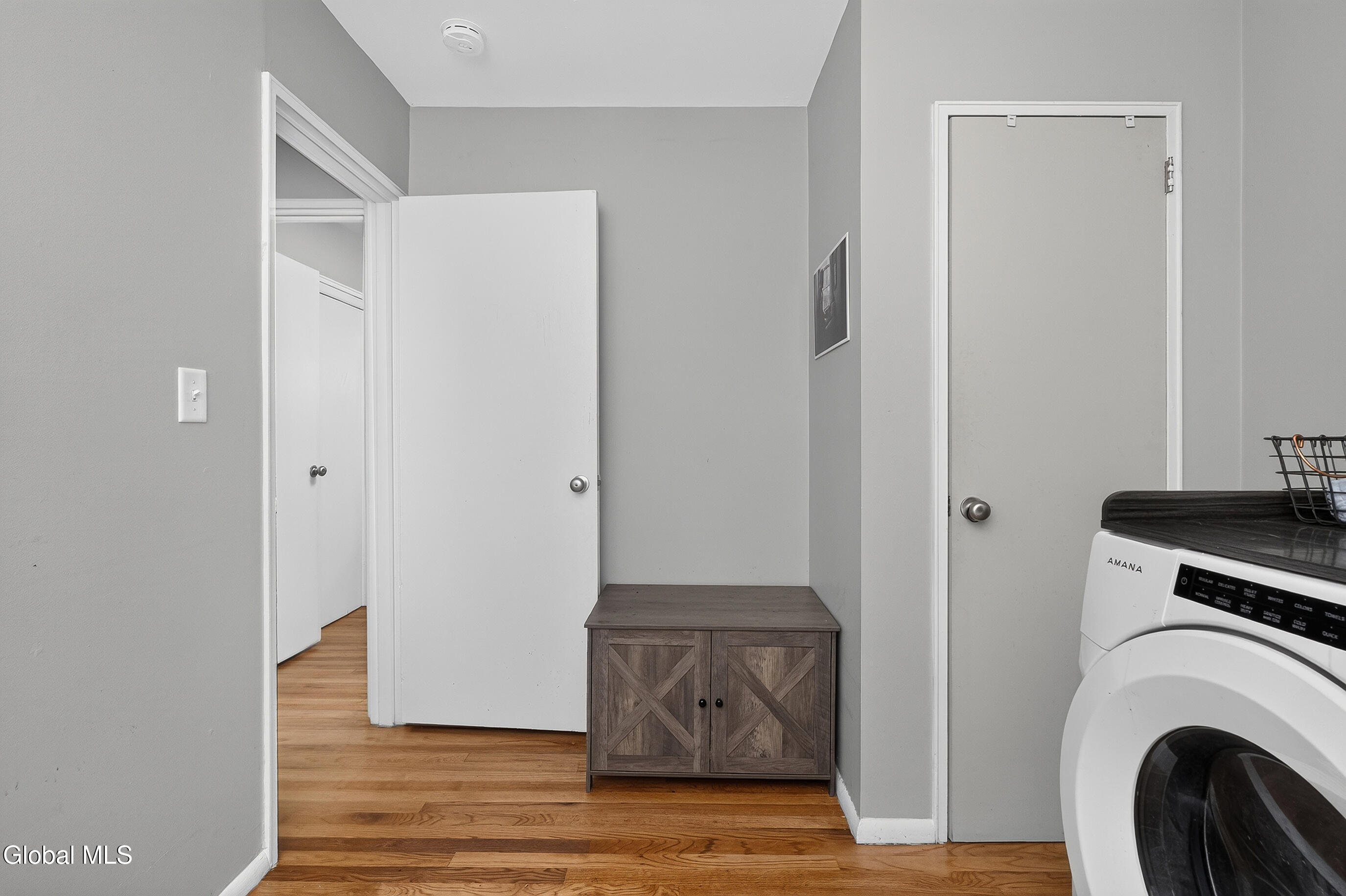 Laundry area with a front-loading washer, wood cabinet, and hardwood floors.