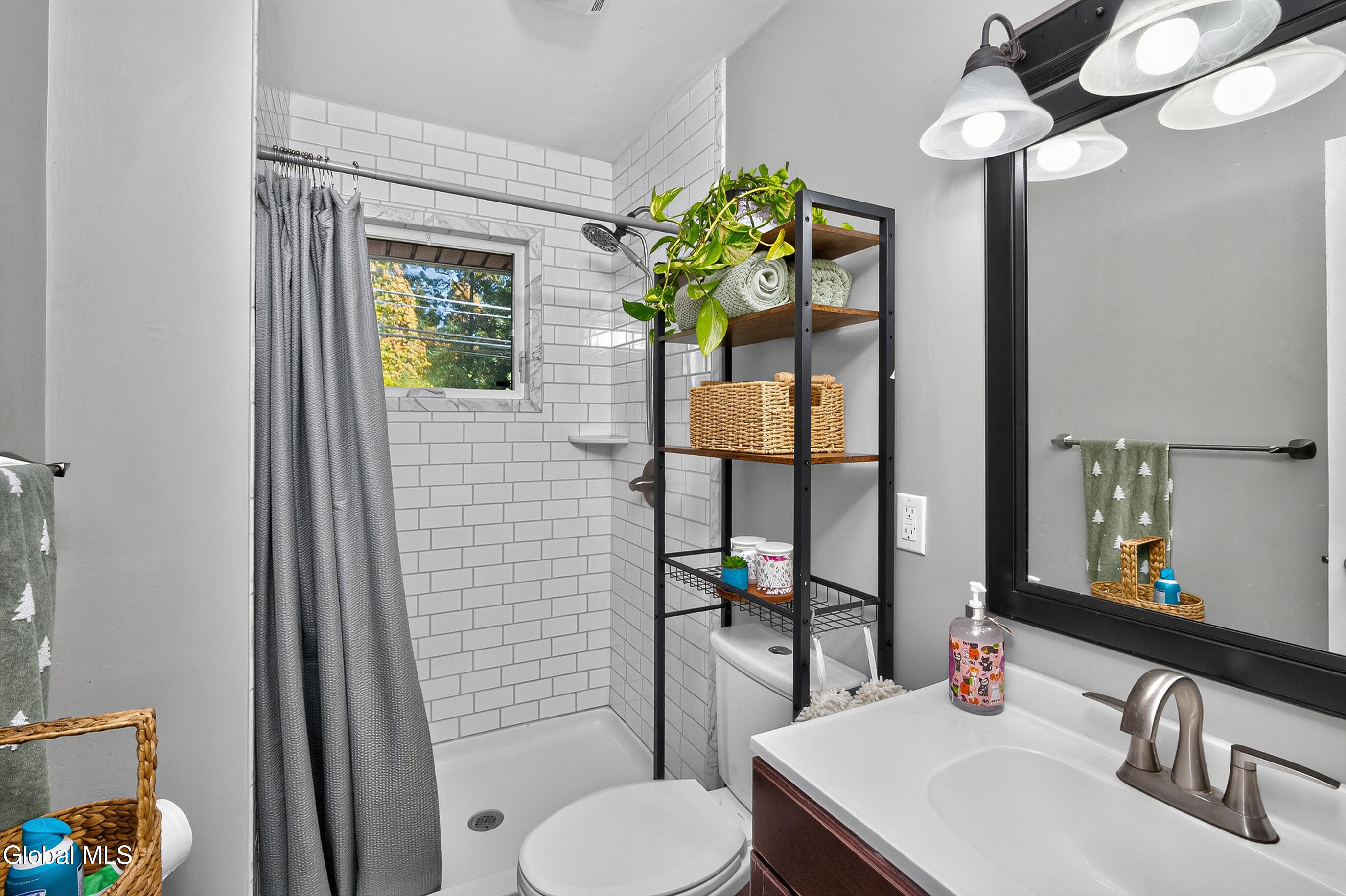 Bathroom with white subway-tile shower, gray curtain, and vanity beneath a large black-framed mirror.