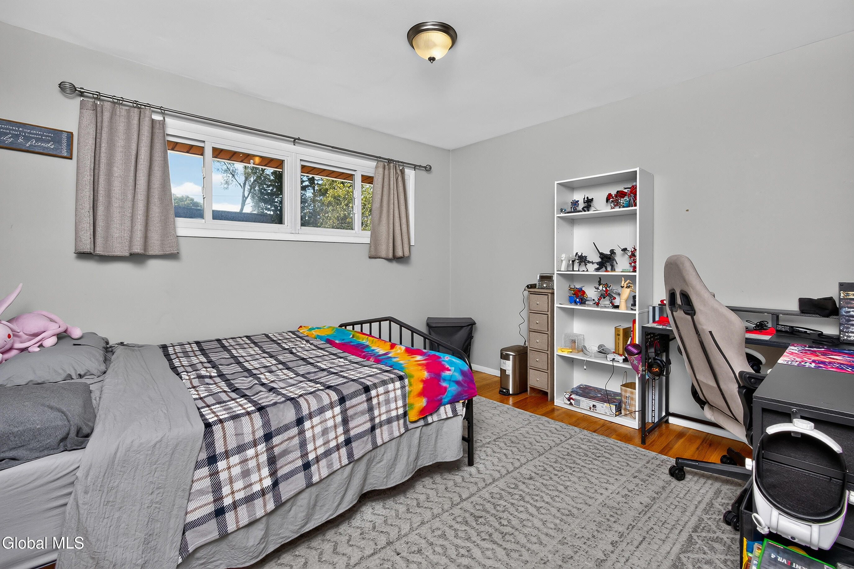 Bedroom with plaid bedding, a colorful tie-dye blanket, display shelves, and a gaming desk.
