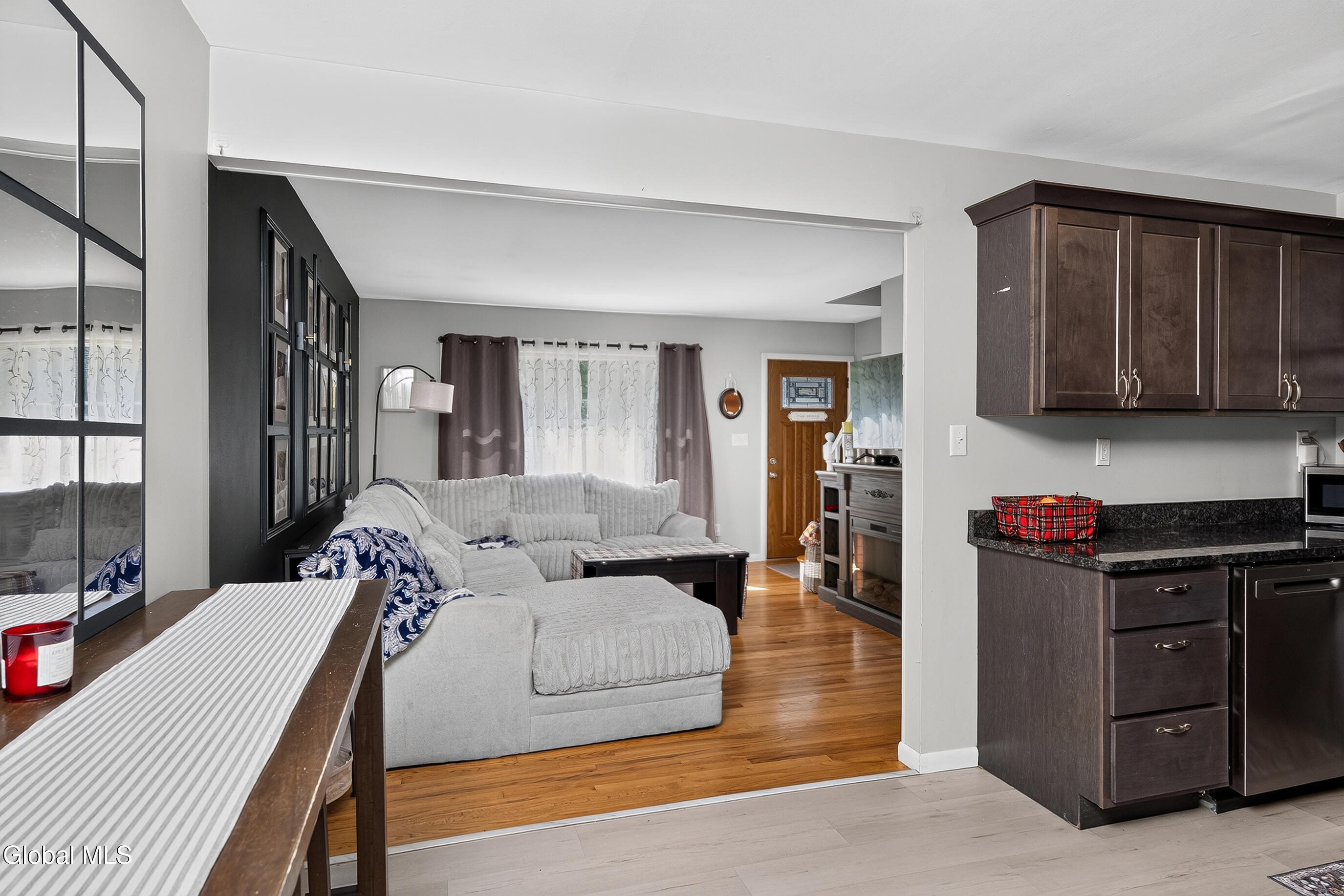Open-plan living room and kitchen with a gray sectional, dark wood cabinets, and hardwood floors.