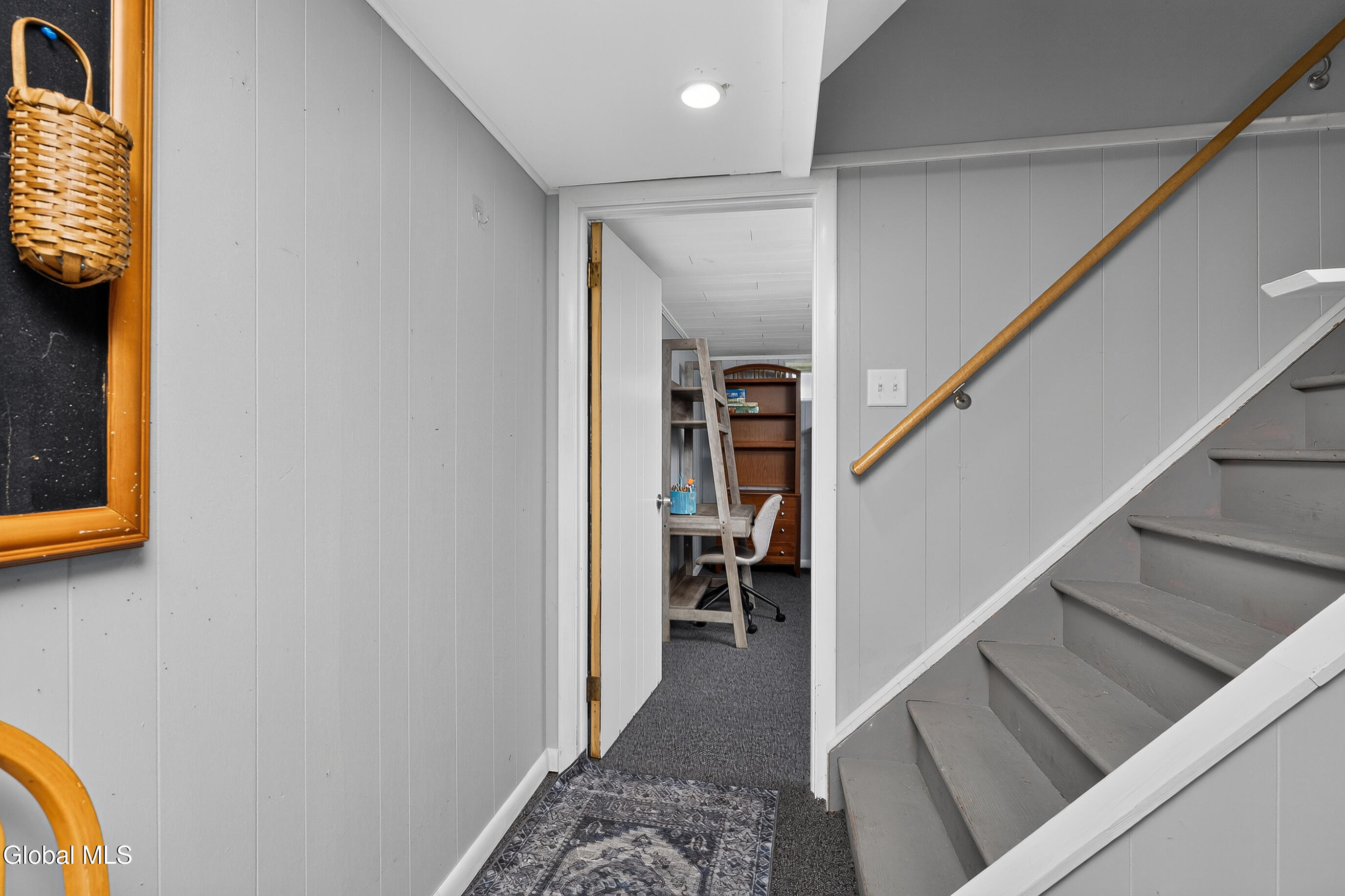Hallway with gray staircase and wooden handrail, opening onto a furnished office.