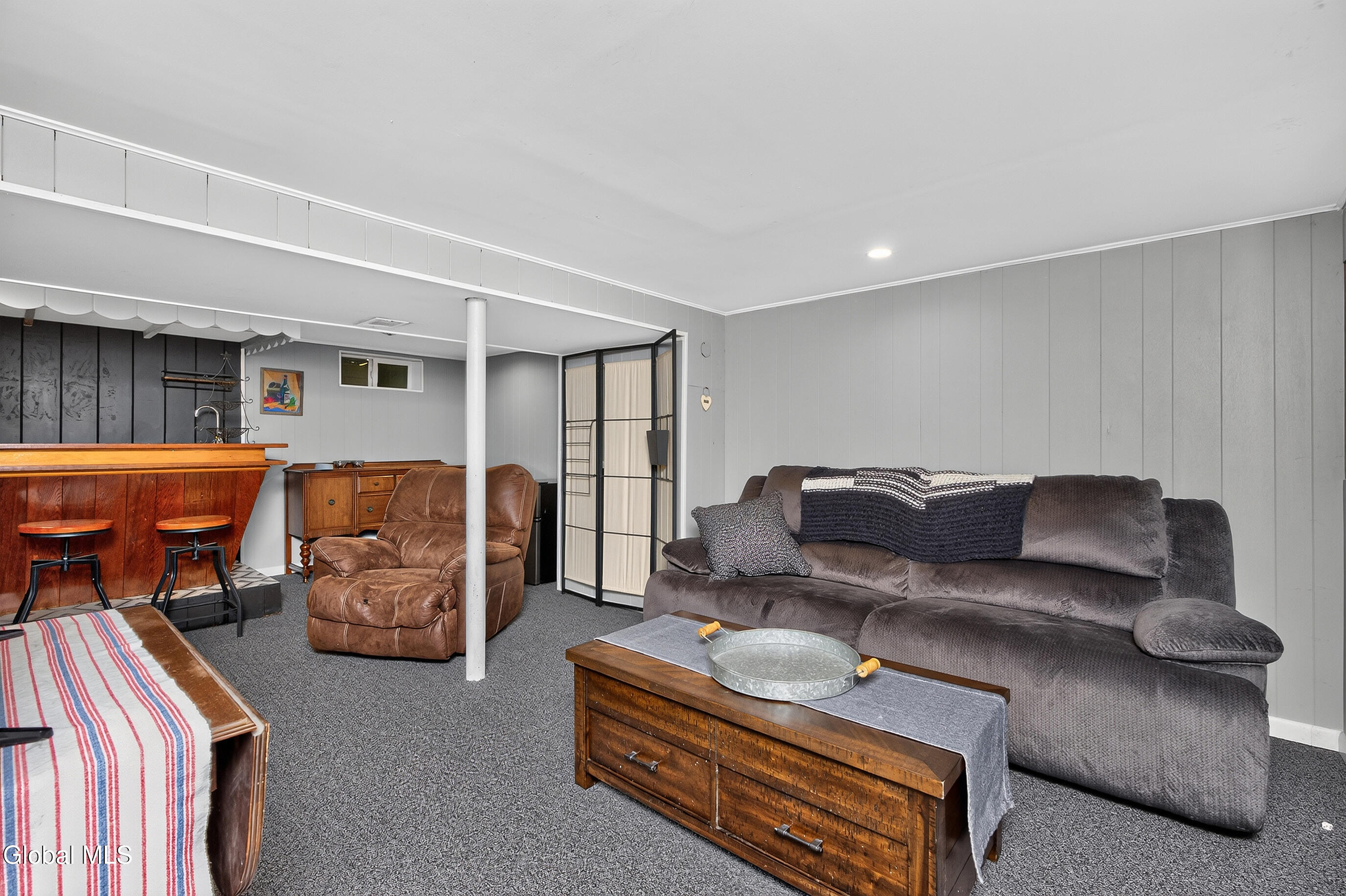 Basement family room with a gray sectional, leather recliner, and wooden bar with stools.
