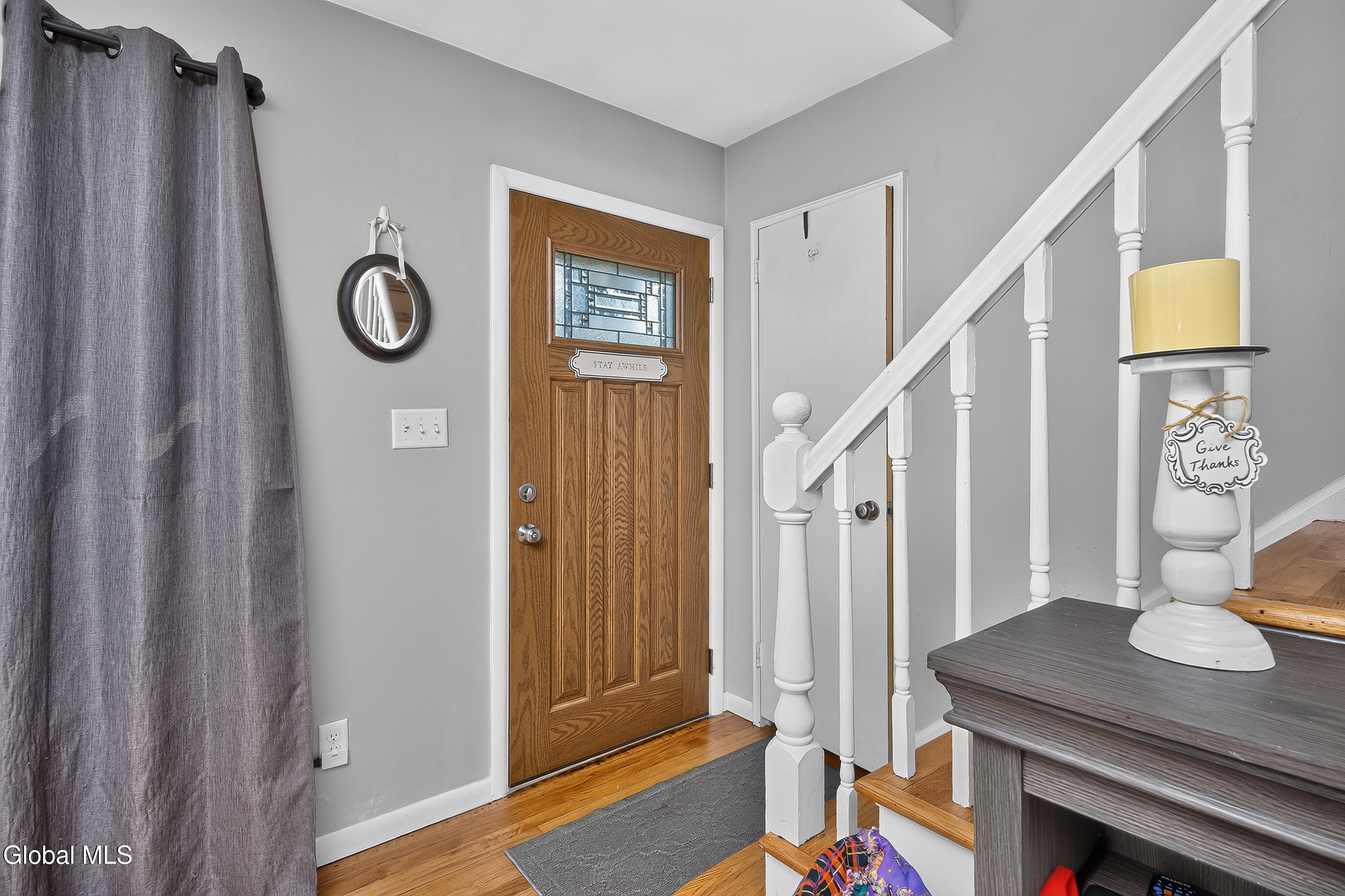 Entry foyer with a stained-glass wooden front door, hardwood floors, and white staircase.