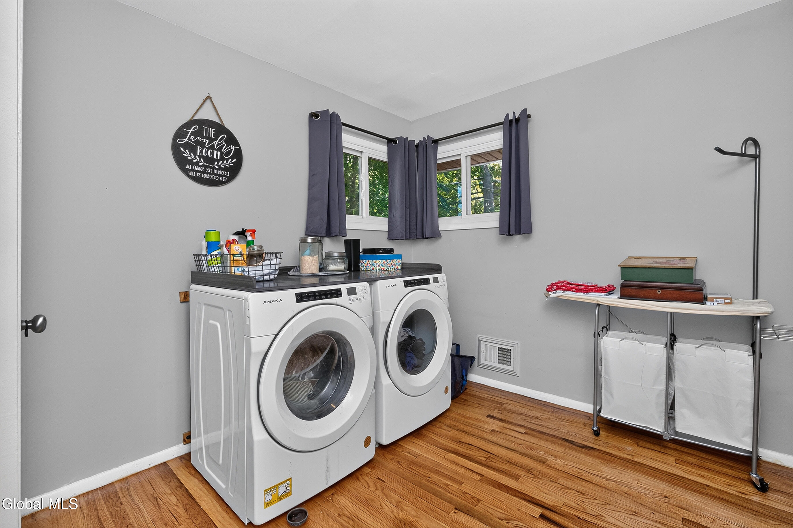 Laundry room with front-loading washer and dryer, curtained windows, and a folding table with hampers.