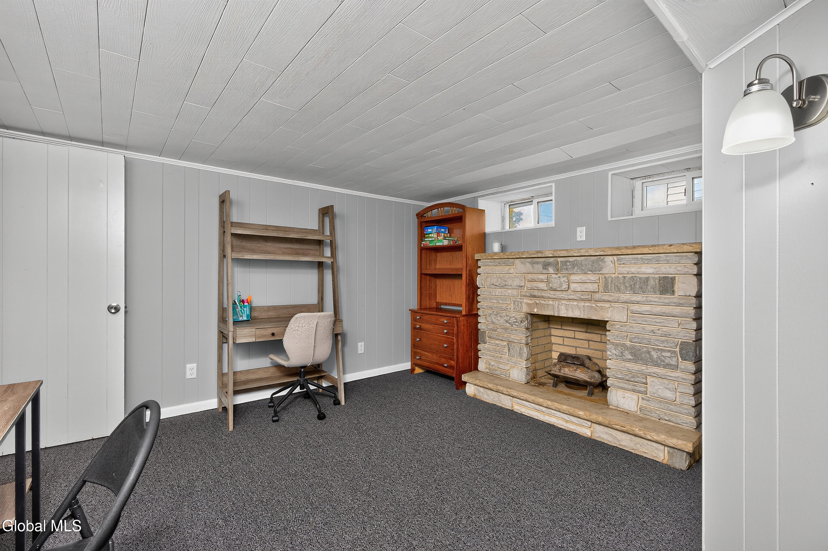 Furnished room with a stone fireplace, desk and chair, and gray paneled walls.