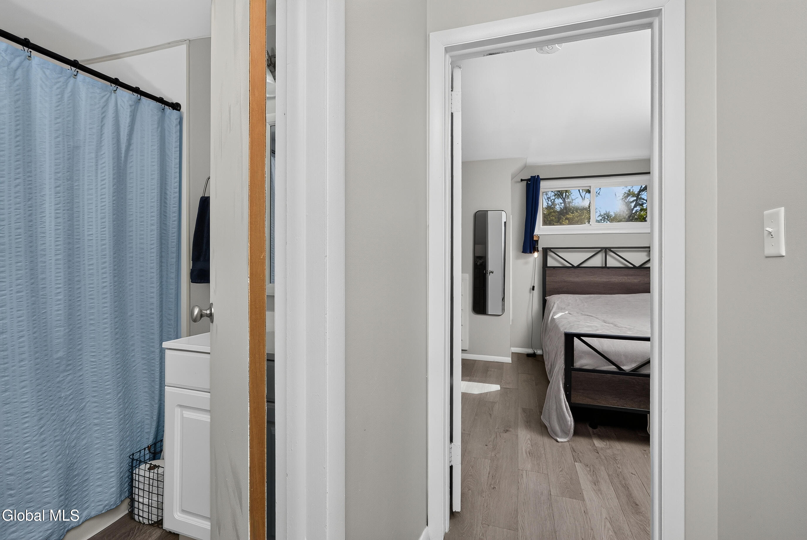 Bathroom with blue shower curtain and vanity opening onto a bedroom with a black metal bed.