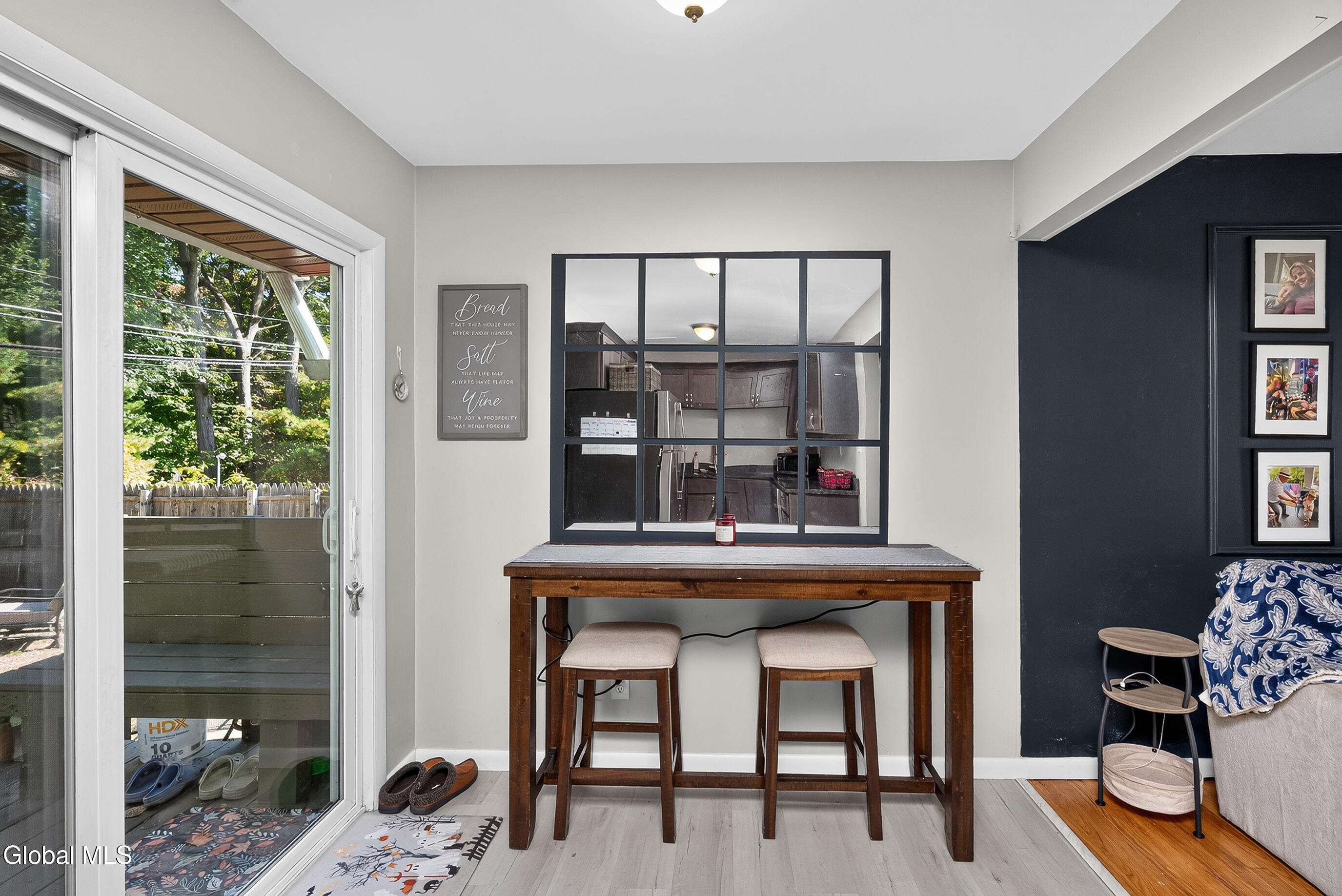 Dining nook with a wooden table and stools, kitchen pass-through, and sliding door to a leafy backyard.