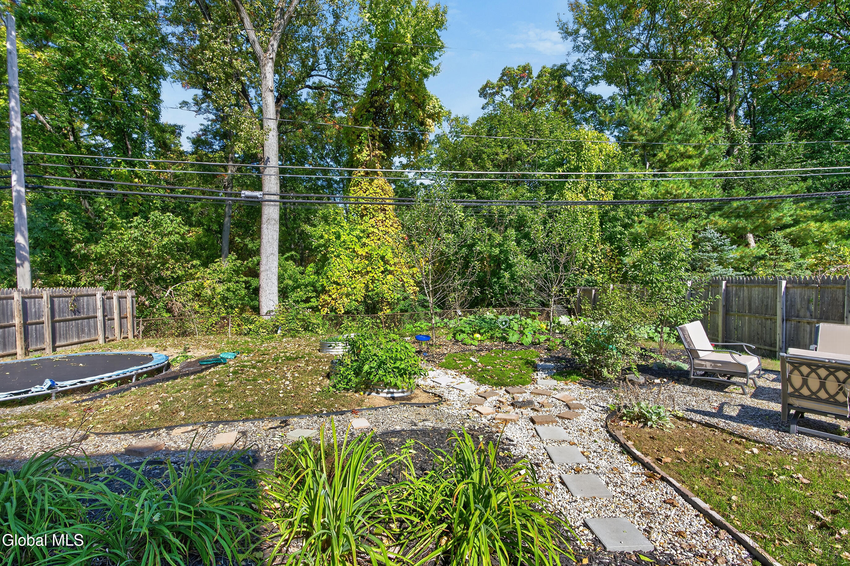 Landscaped backyard with a gravel stepping-stone path, garden beds, outdoor chairs, and a trampoline.