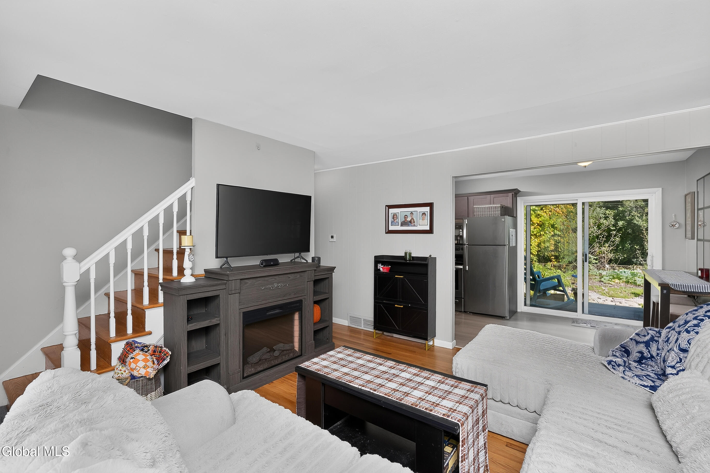 Living room with white sofas, a dark wood fireplace, staircase, and sliding doors to the yard.
