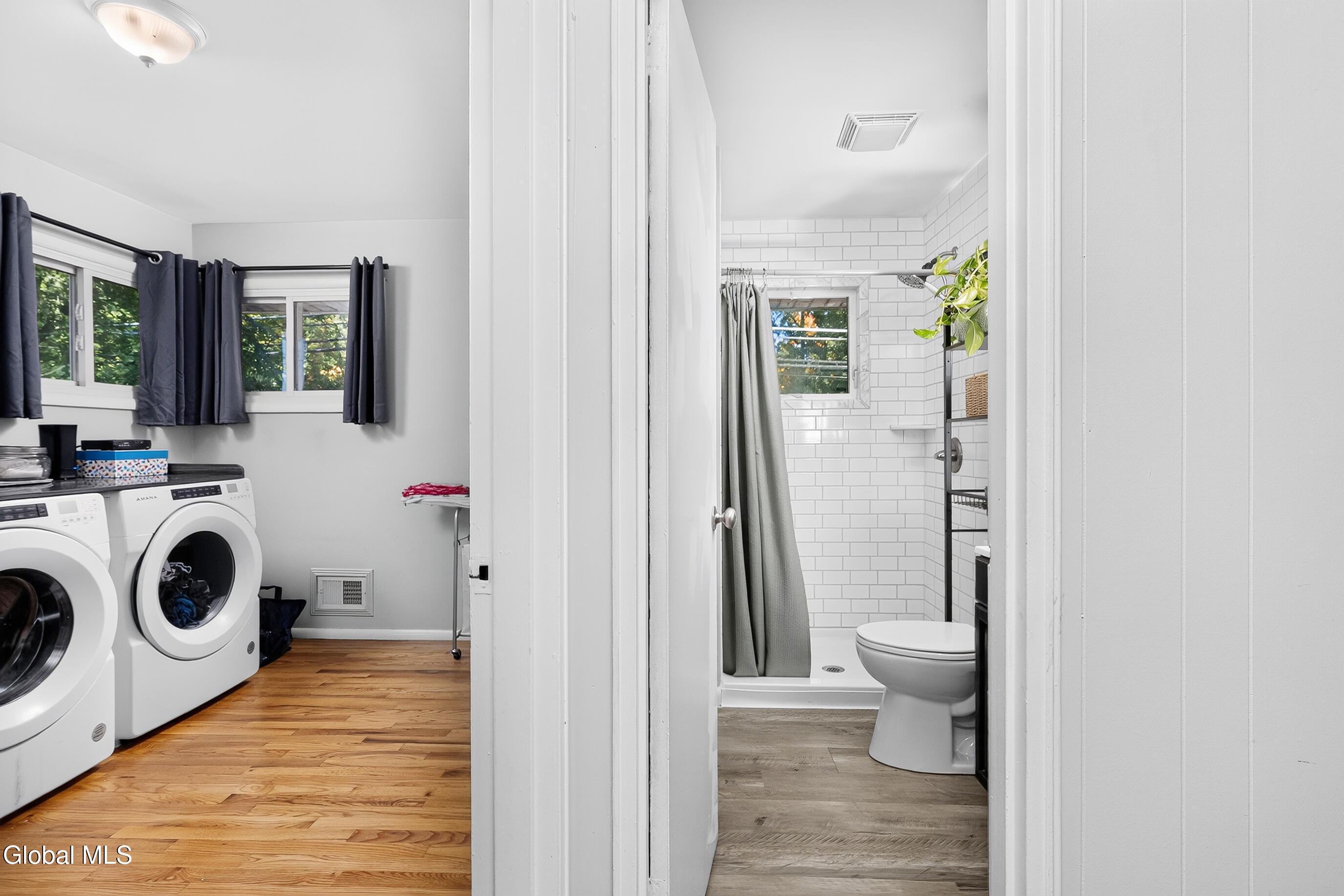 Laundry room with front-loading machines opens onto a subway-tile bathroom.