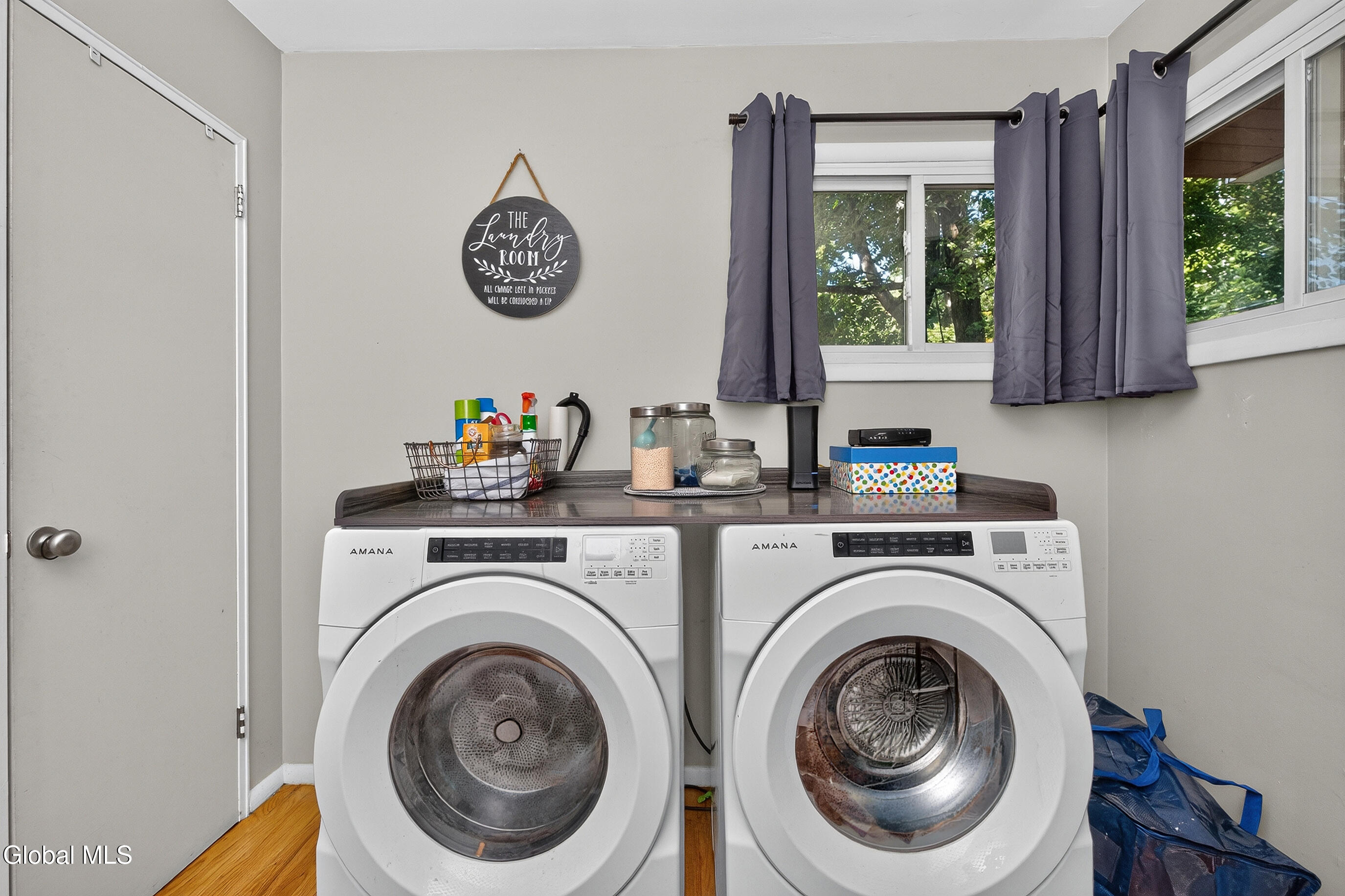 Laundry room with two front-loading machines, a dark countertop, and a window with gray curtains.