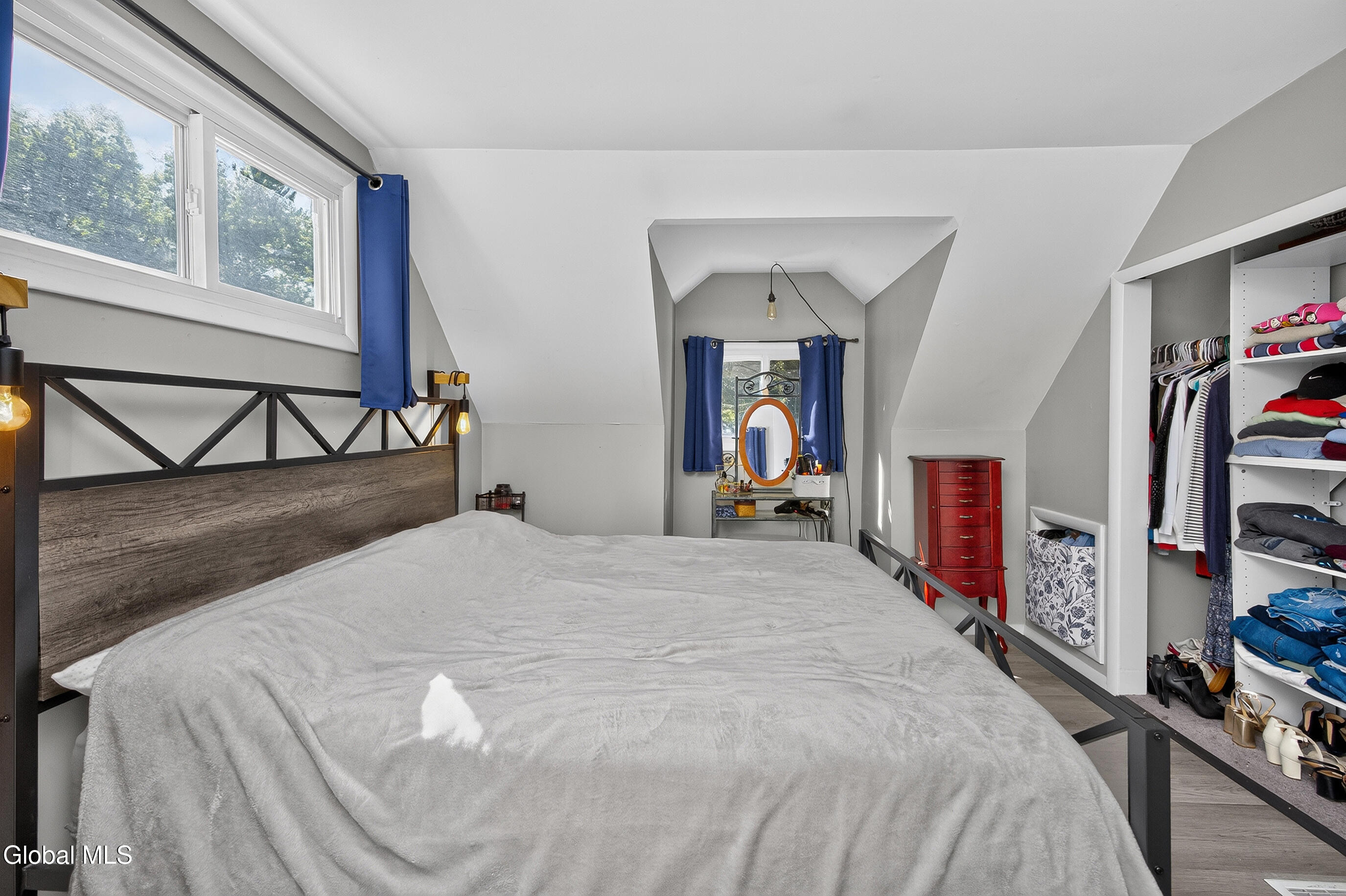 Bedroom with a large bed, blue curtains, and an open closet beneath a sloped ceiling.