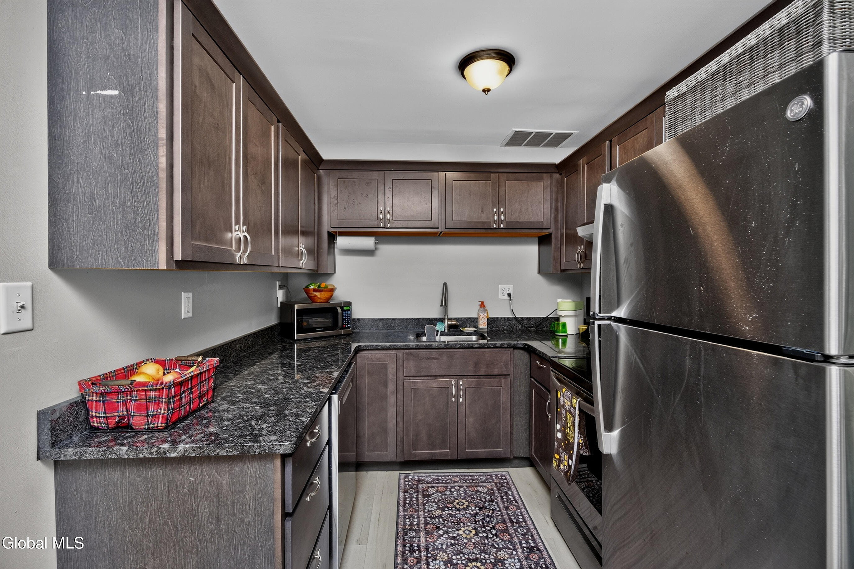 Galley kitchen with dark cabinets, black countertops, stainless-steel appliances, and a patterned floor runner.