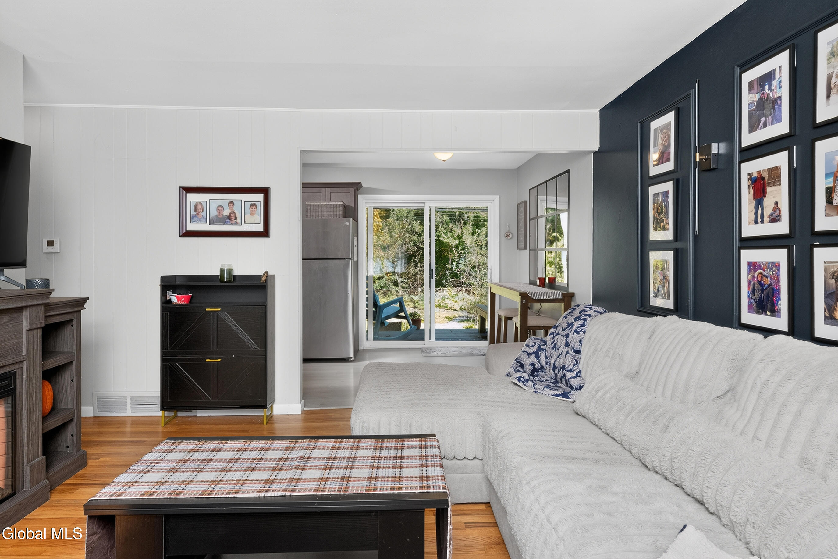 Living room with a white sectional, dark blue gallery wall, and sliding doors to a green backyard.