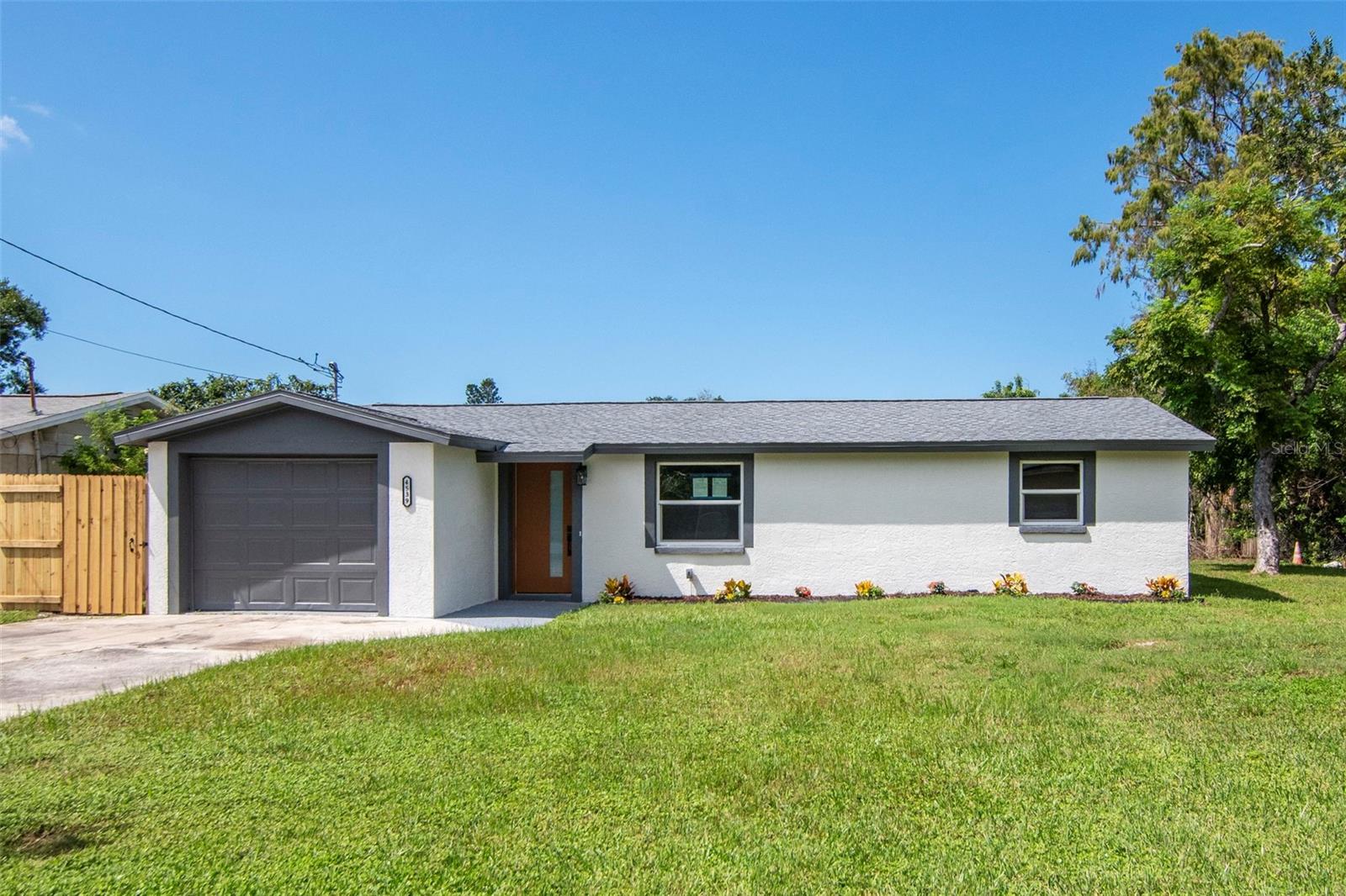 Single-story home with a gray garage door, light stucco exterior, and a broad front lawn.