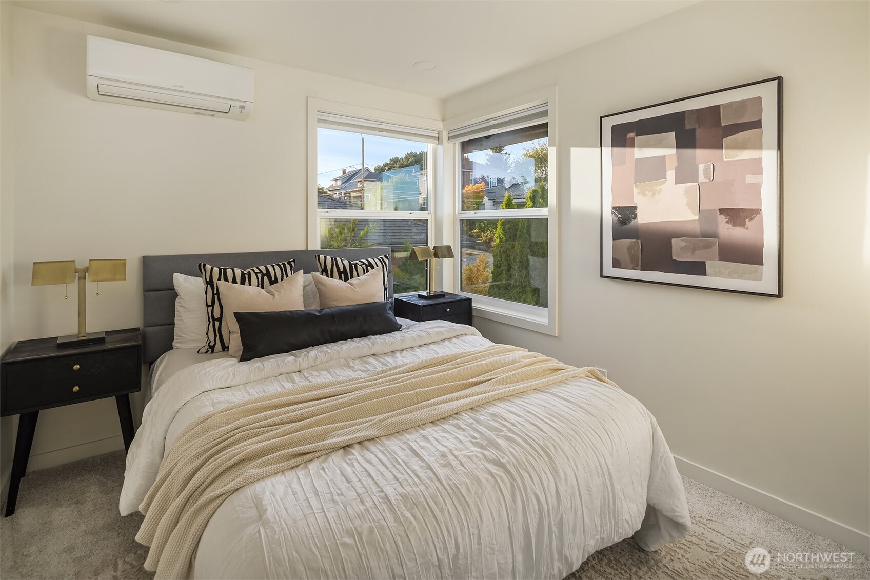 Staged bedroom with a white quilted bed, corner windows, and abstract wall art.