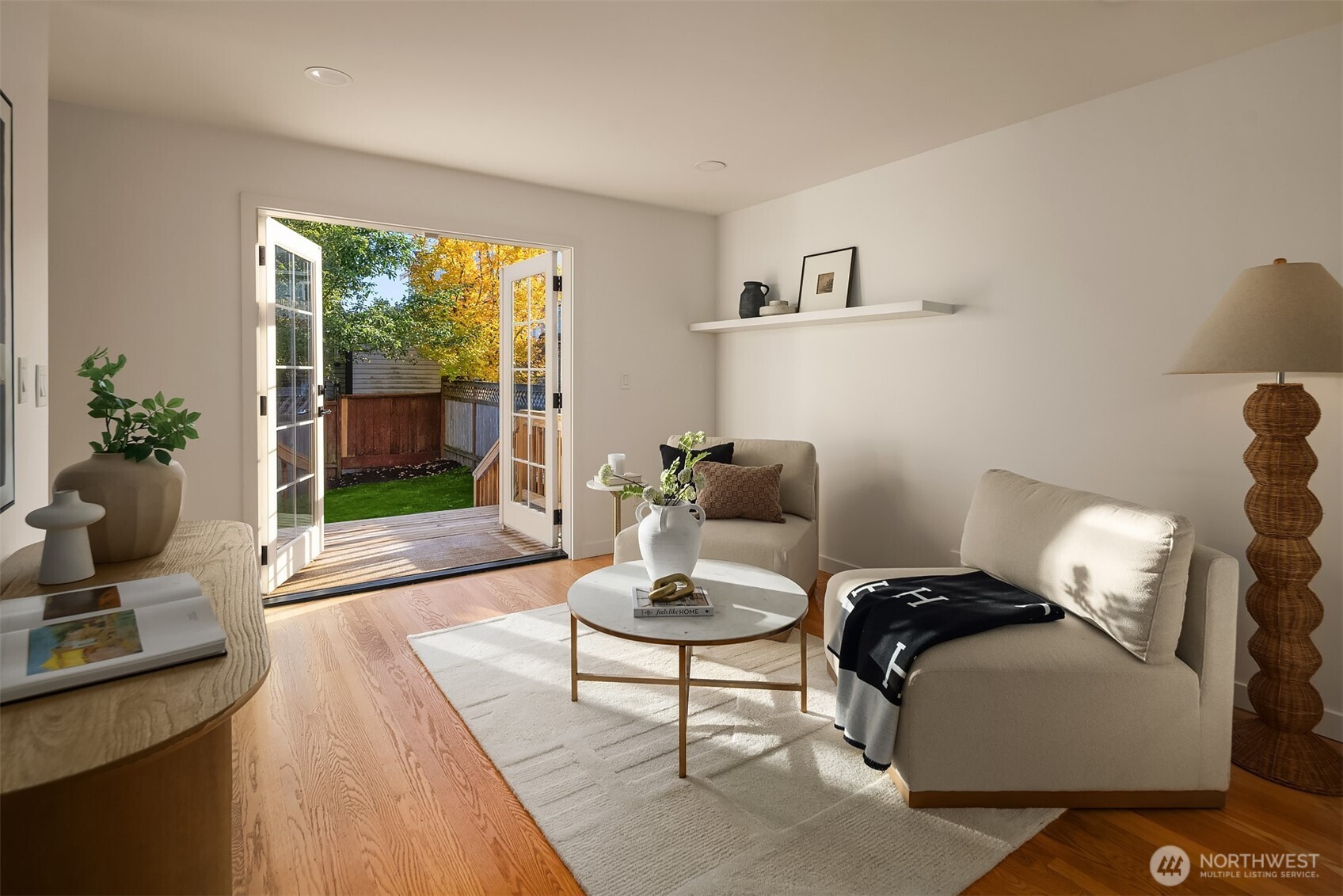 Staged living room with hardwood floors and open French doors to a fenced backyard.