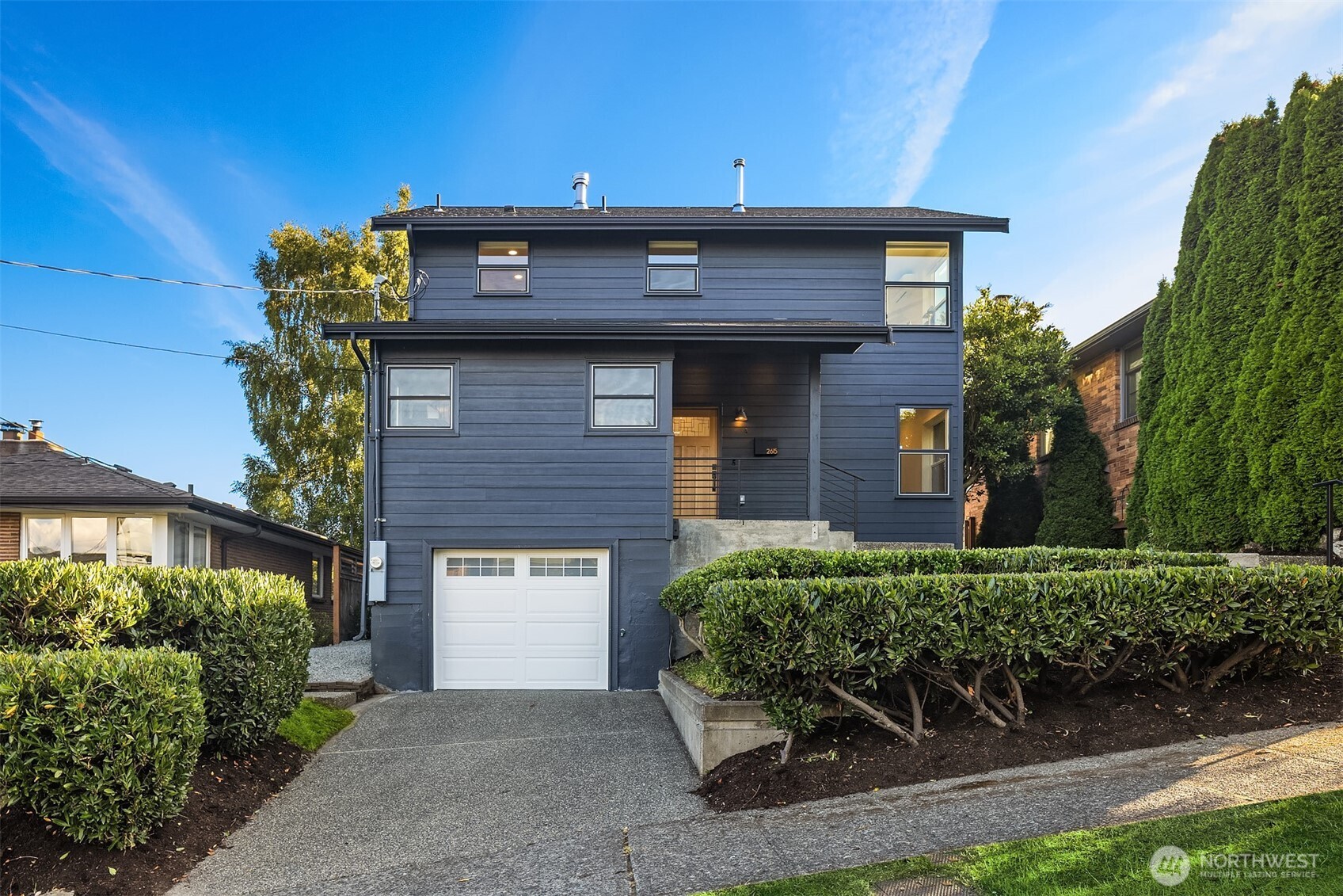 Modern dark blue two-story house with a white garage door and neatly trimmed front hedges.