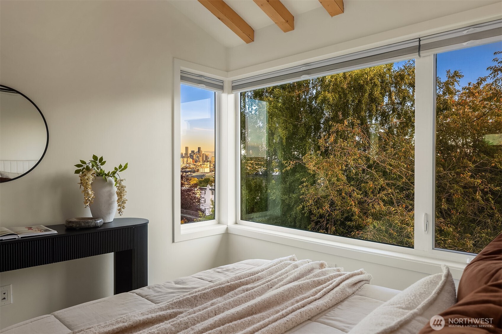 Bedroom with large corner windows overlooking leafy trees and the Seattle skyline.