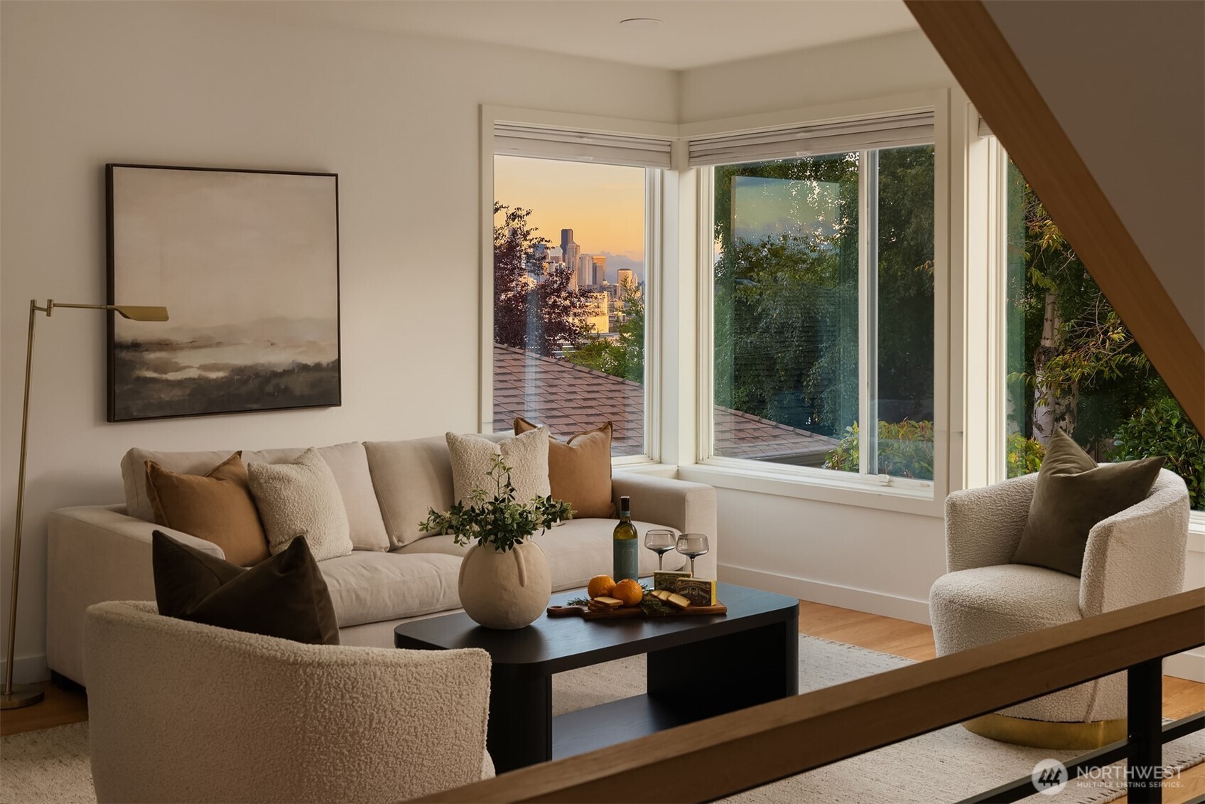Staged living room with corner windows framing the Seattle skyline at sunset.