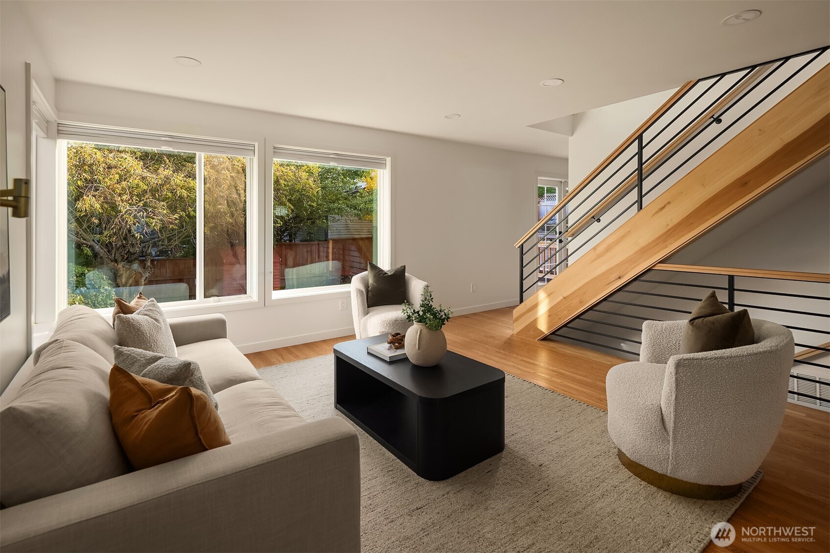 Staged living room with large garden-facing windows and a striking wood-and-black-metal staircase.