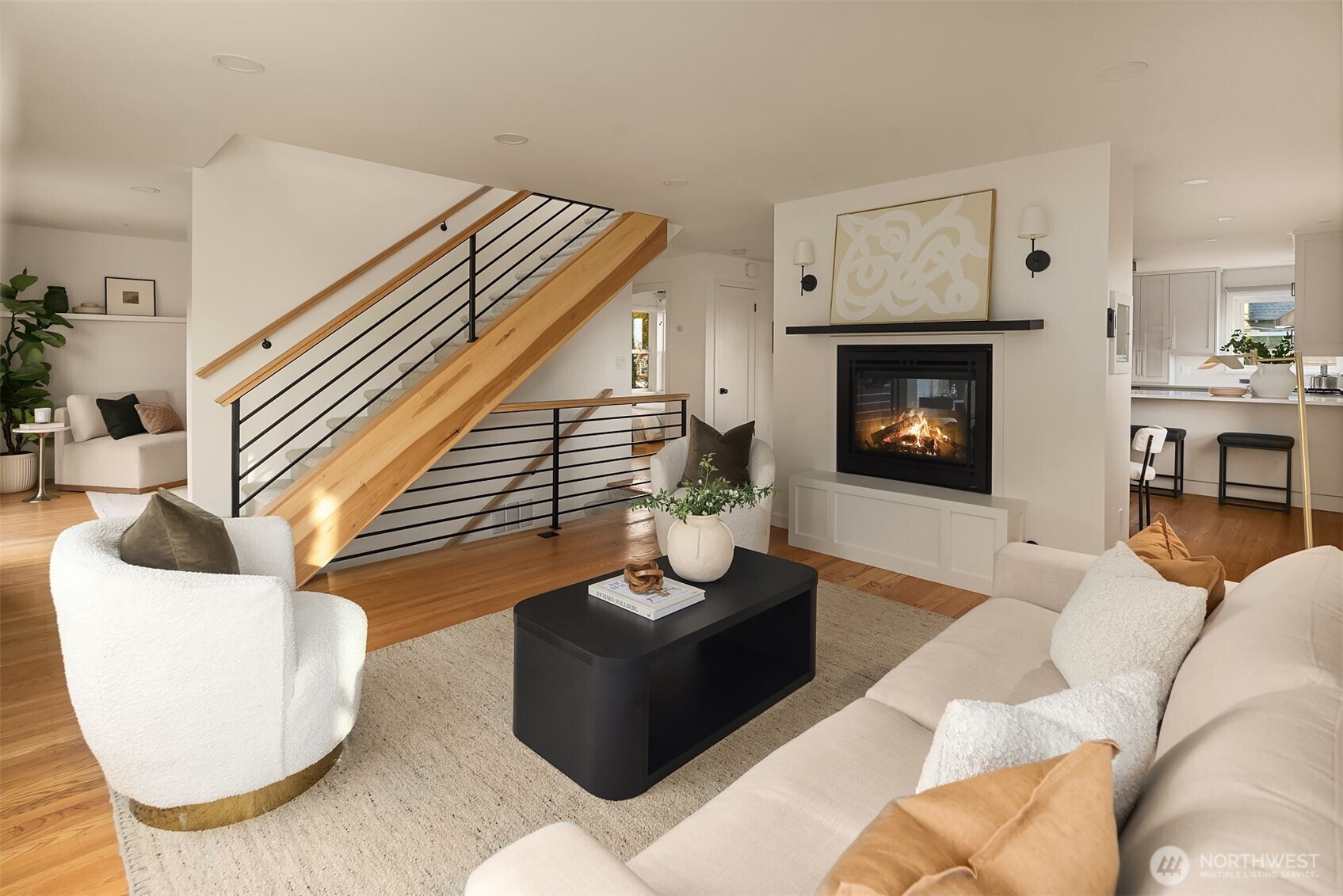 Staged living room with a fireplace, striking wood staircase, and open view into the kitchen.