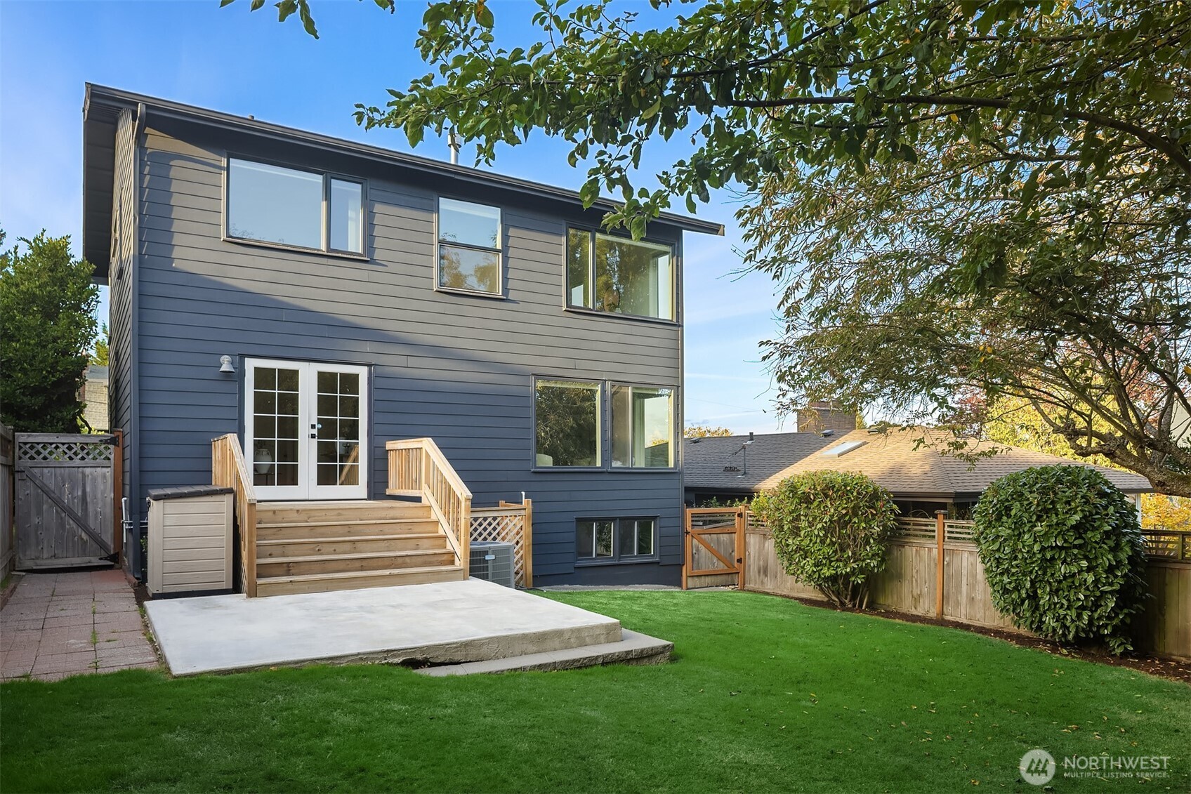 Rear exterior of a dark blue-gray two-story home with wooden steps, a patio, and a fenced lawn.