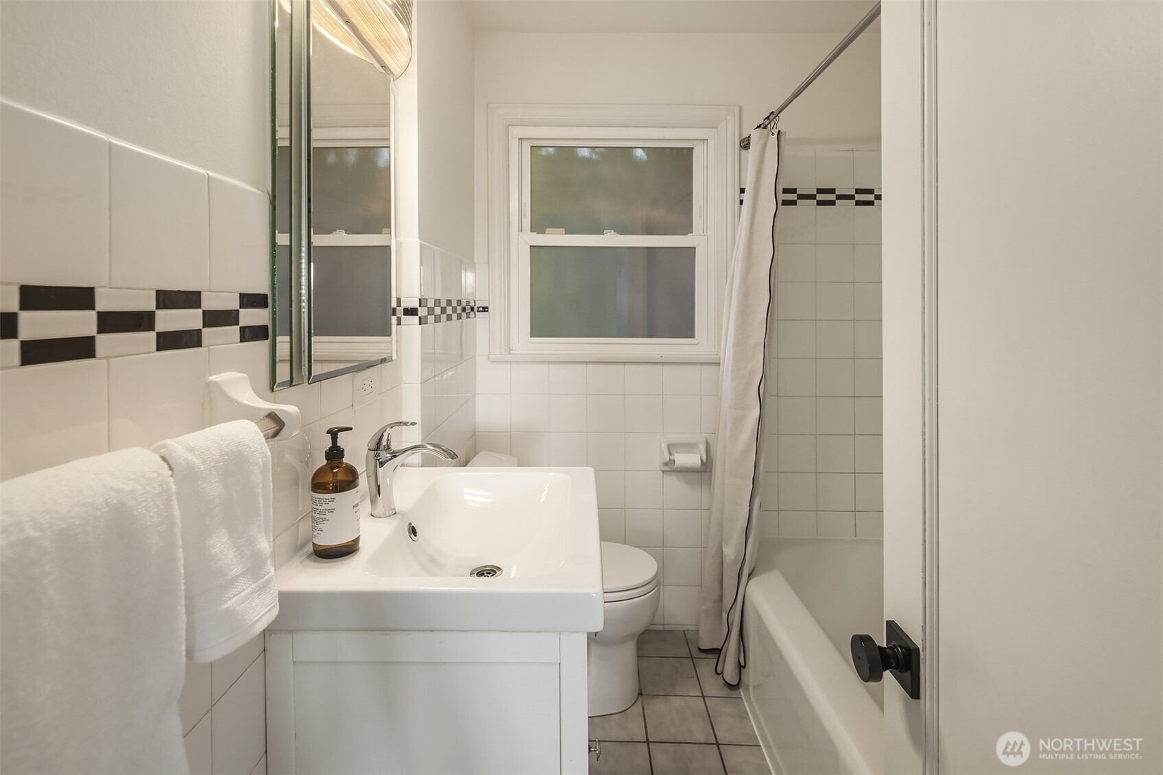 Bathroom with white tiled walls, a black-and-white accent stripe, and a tub-shower.