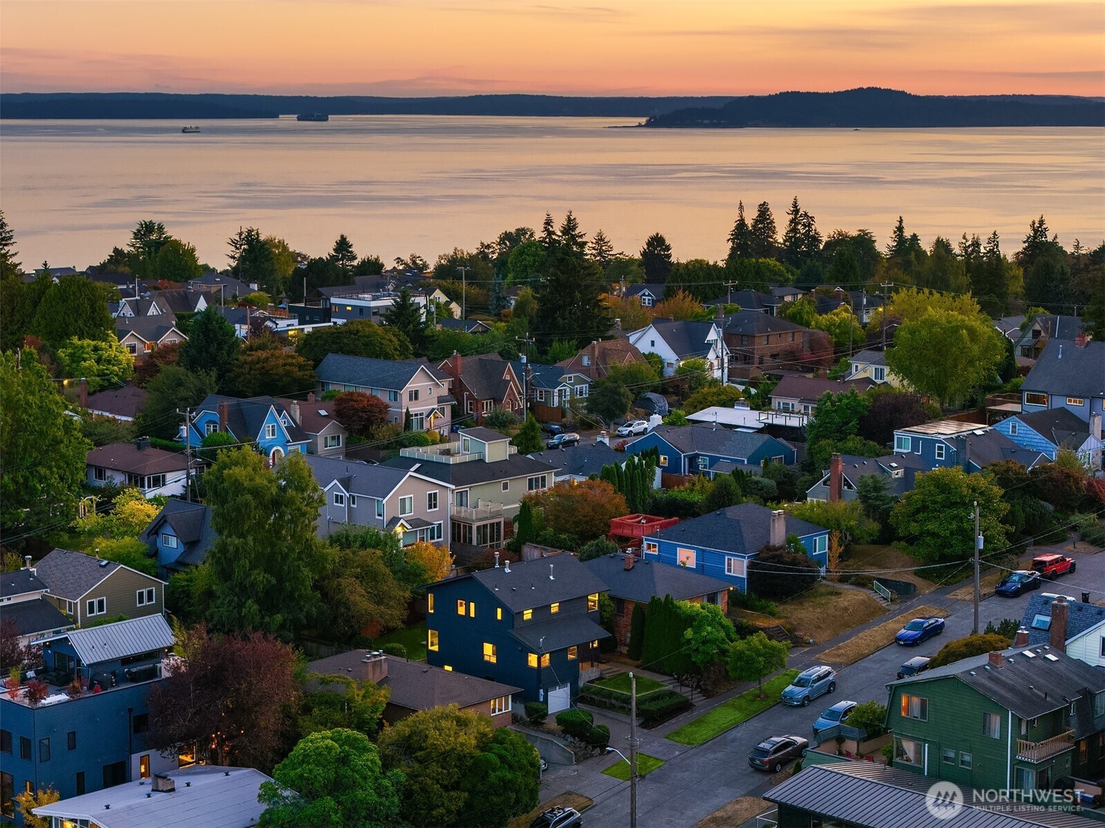 Aerial view of a Seattle neighborhood, with calm water and a wooded shoreline glowing in the sunset.