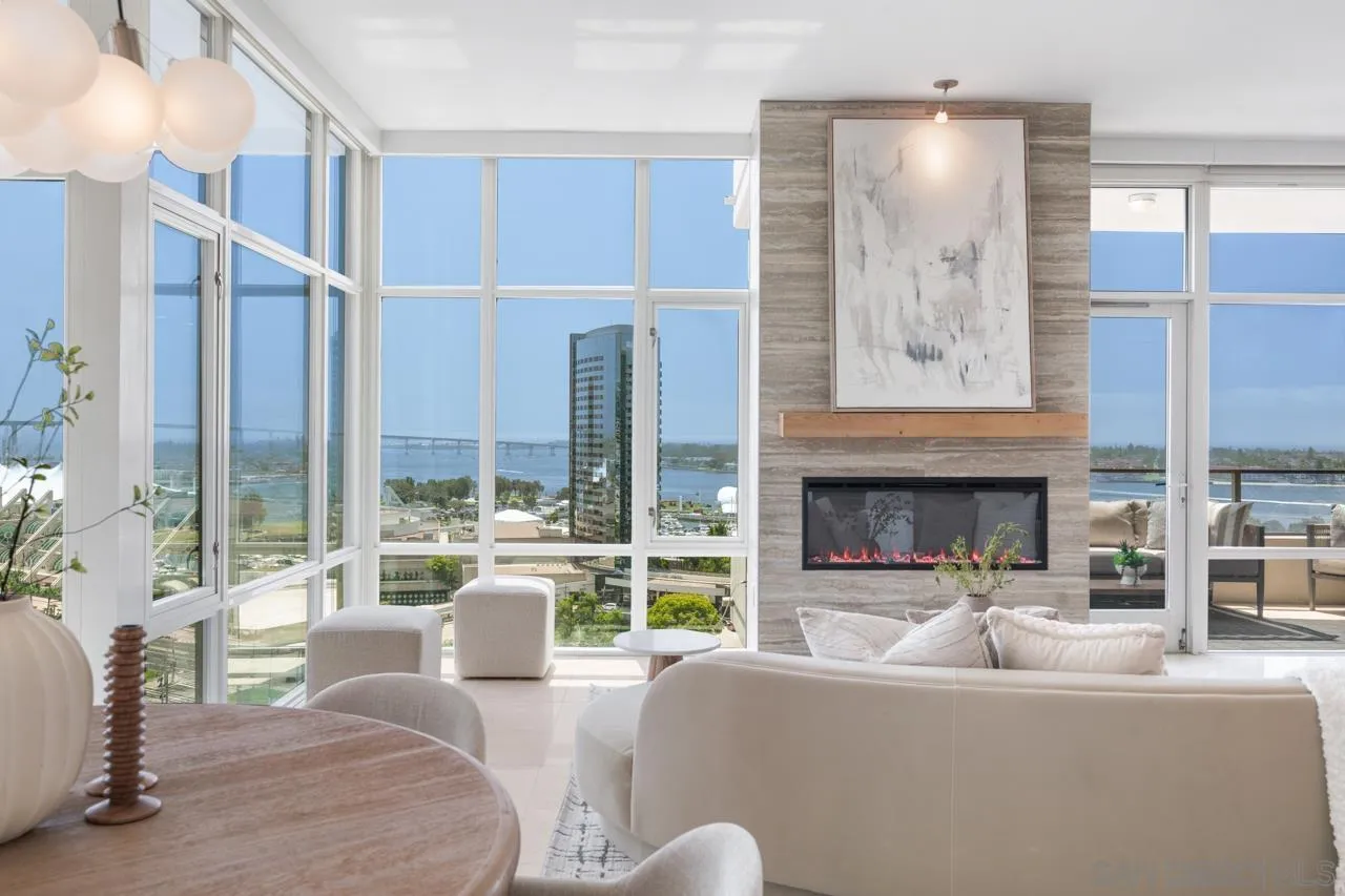 Furnished living room with floor-to-ceiling windows overlooking the bay and bridge, and a marble fireplace.