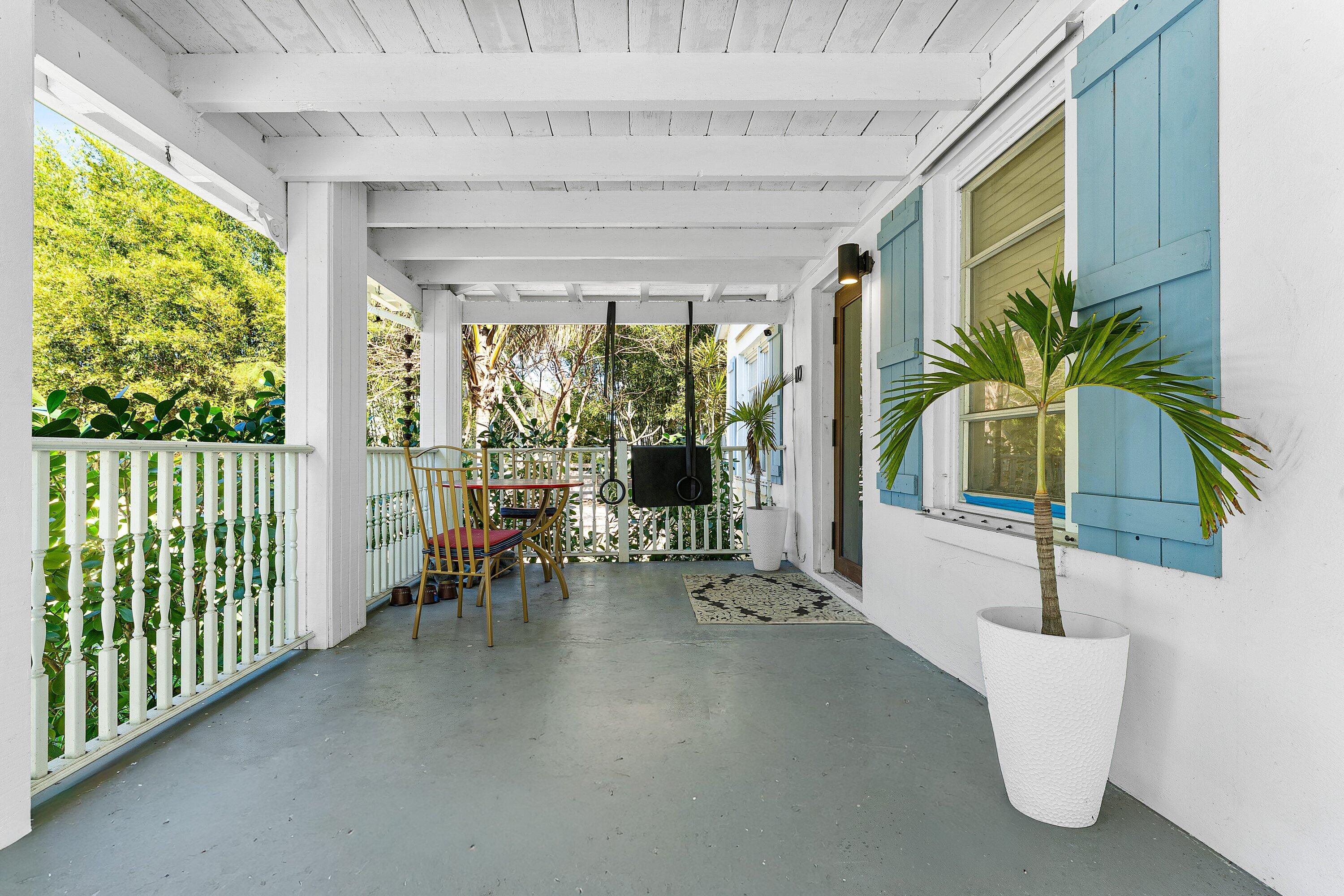 Covered porch with blue shutters, a hanging swing, and potted palms.