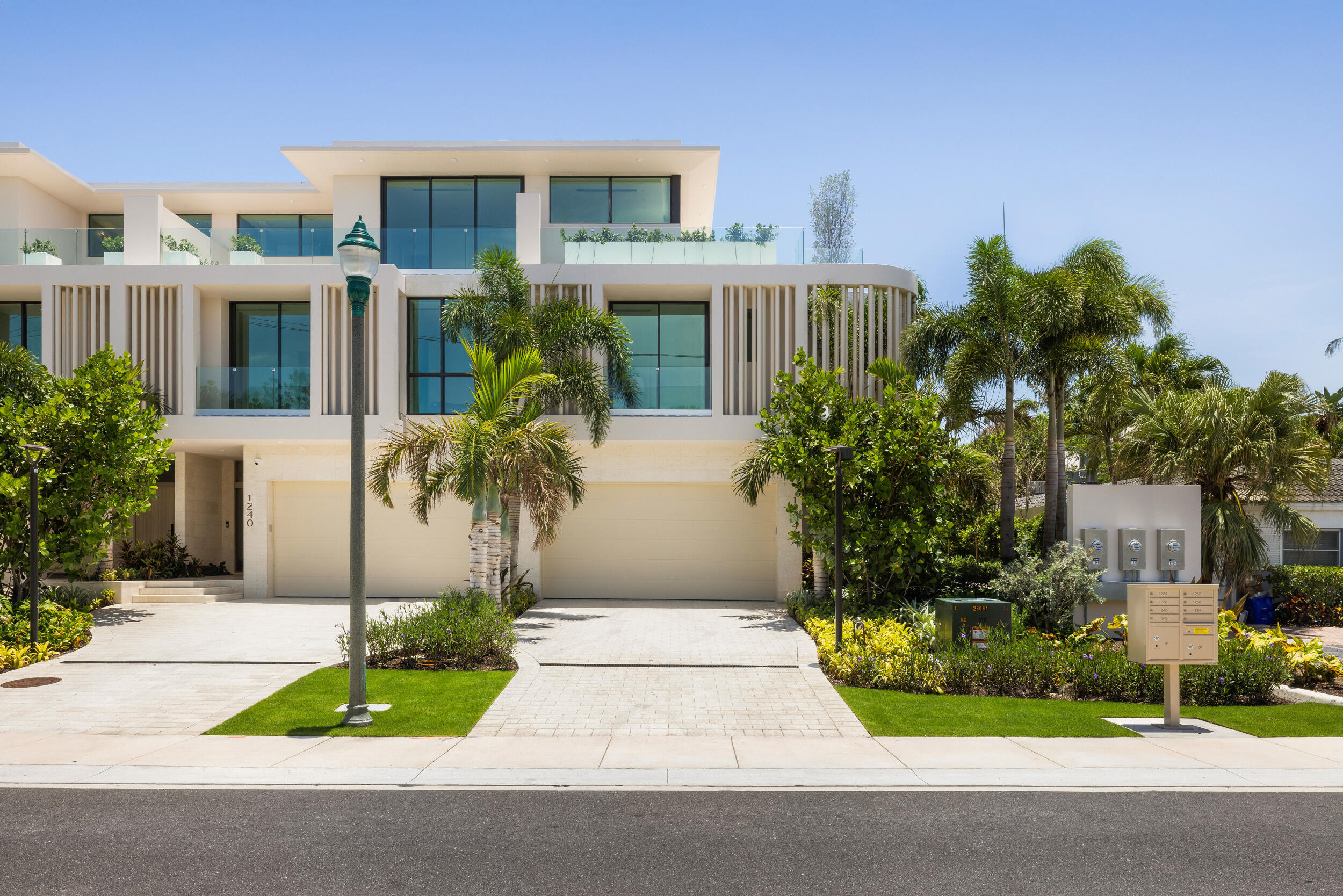 Modern white home with glass balconies, two garage doors, tropical landscaping, and the number 1240 beside the entrance.