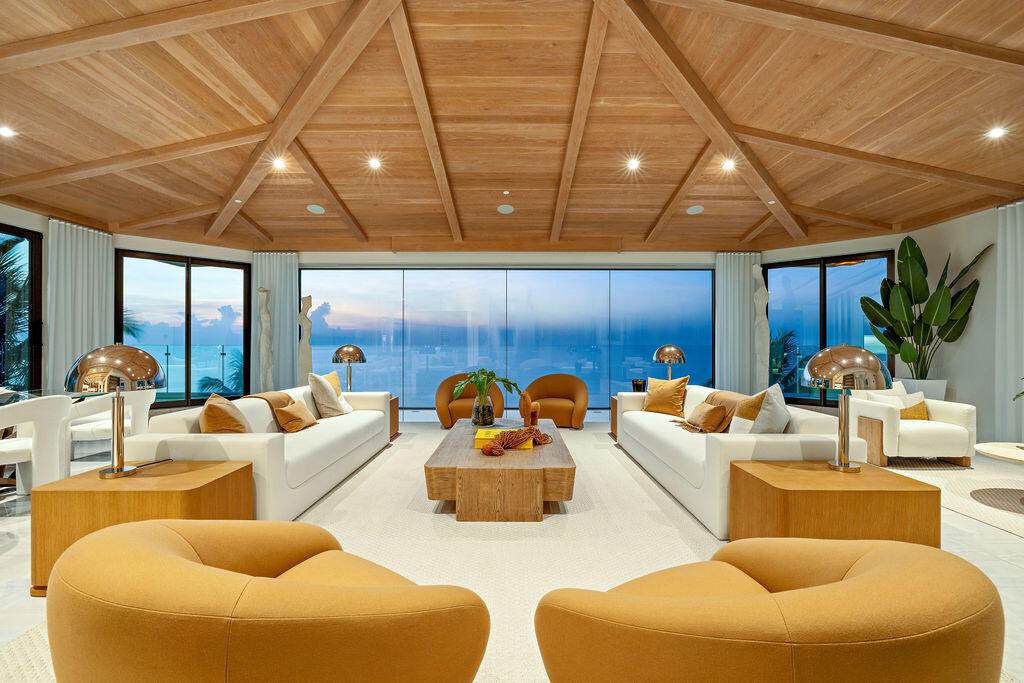 Living room with a sculptural wood ceiling, white sofas, and ocean views through expansive windows.