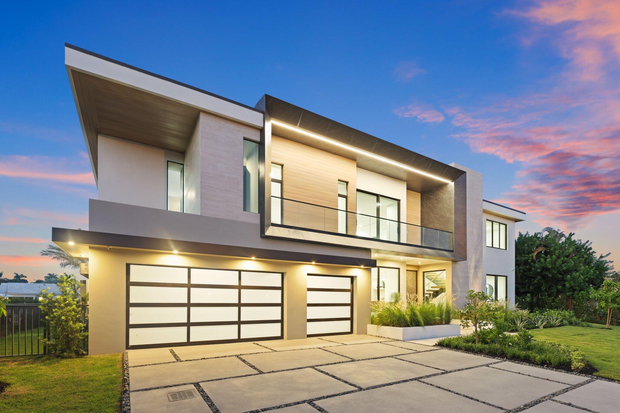 Contemporary two-story home with a glass balcony, twin garages, and landscaped driveway at dusk.