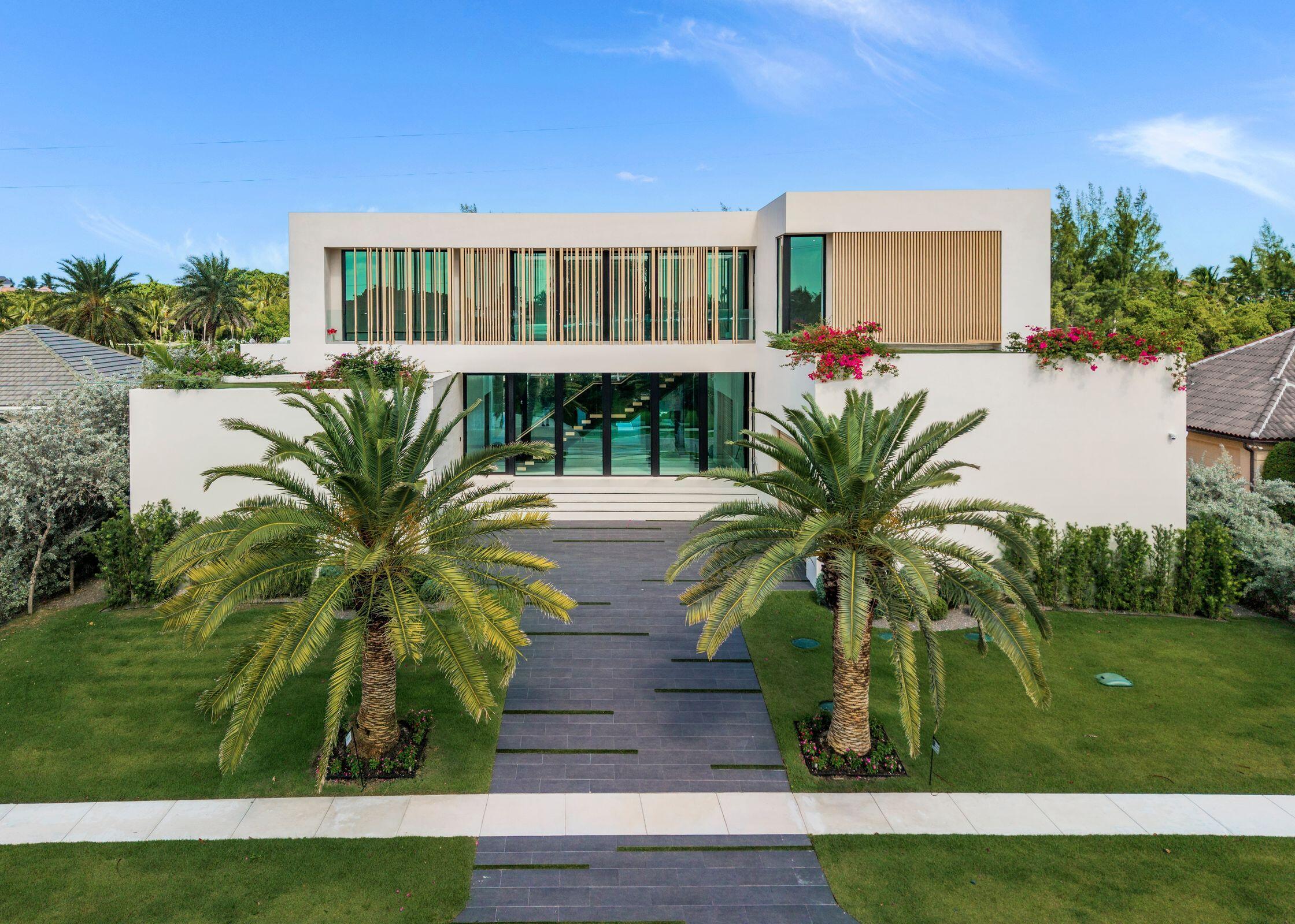 Modern white two-story home framed by palms, with a central paved walkway and vertical wood screens.