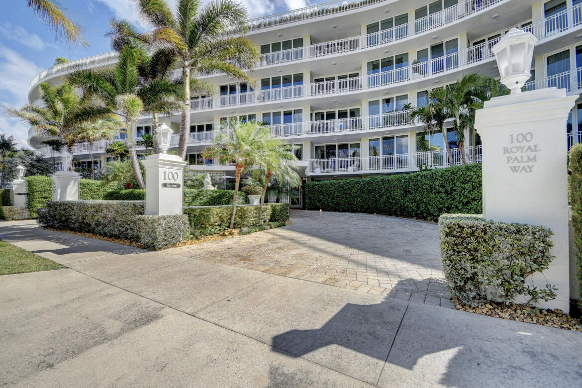 Residential building at 100 Royal Palm Way, with white balconies, palm trees, and a paved entrance.