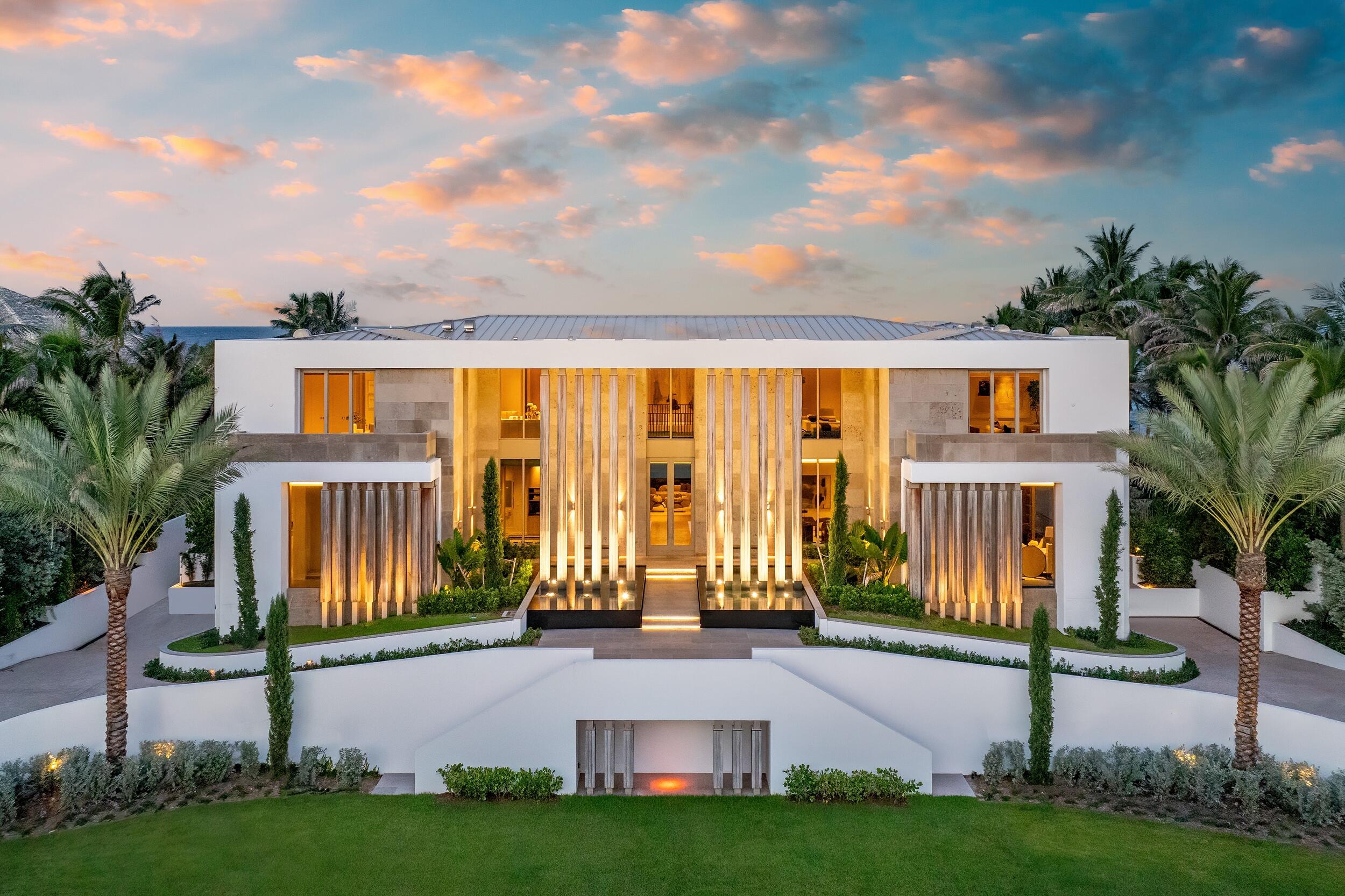 Modern beachfront home with illuminated columns and palm trees at dusk.