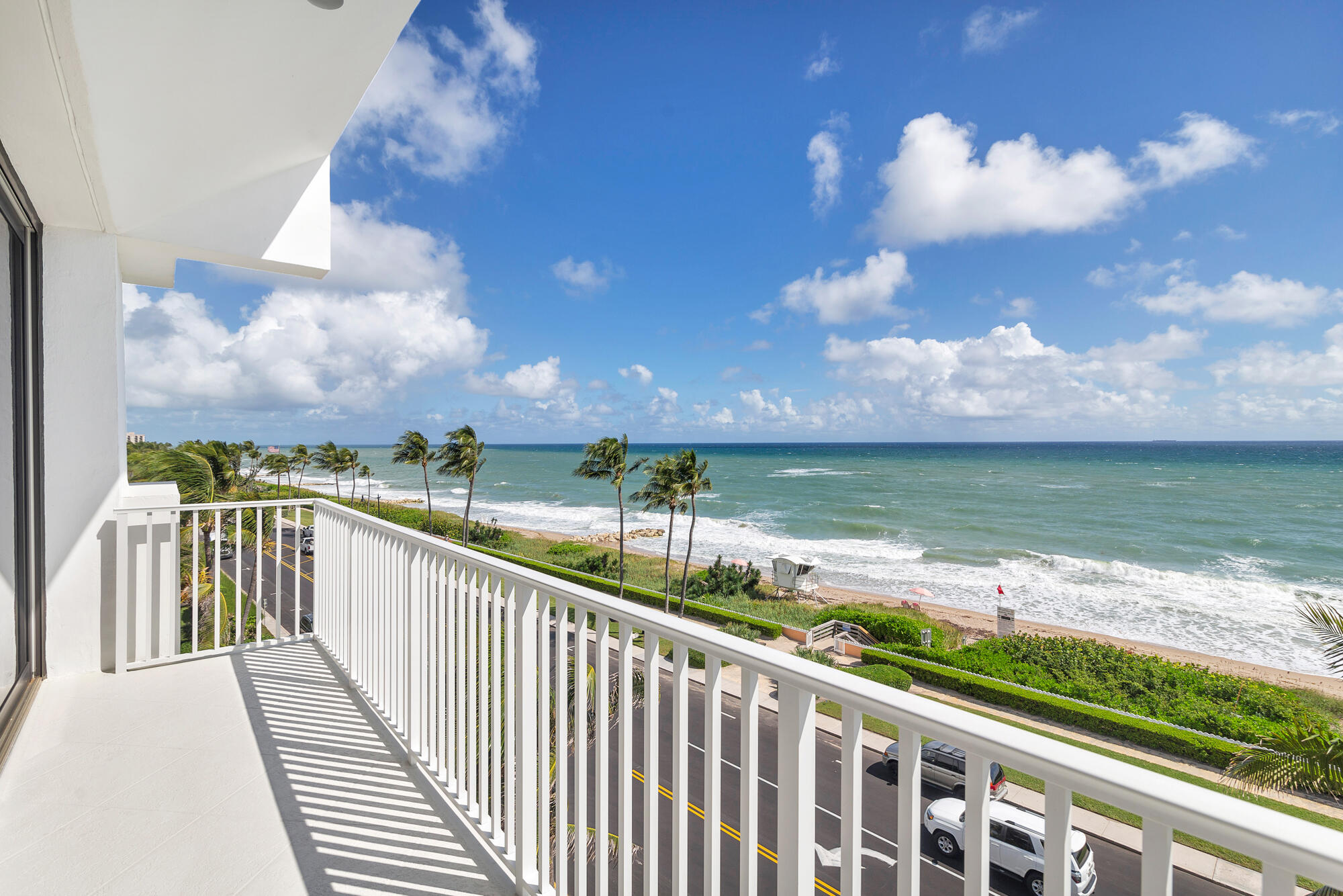 Condominium balcony overlooking palm trees, a sandy beach, and the ocean.