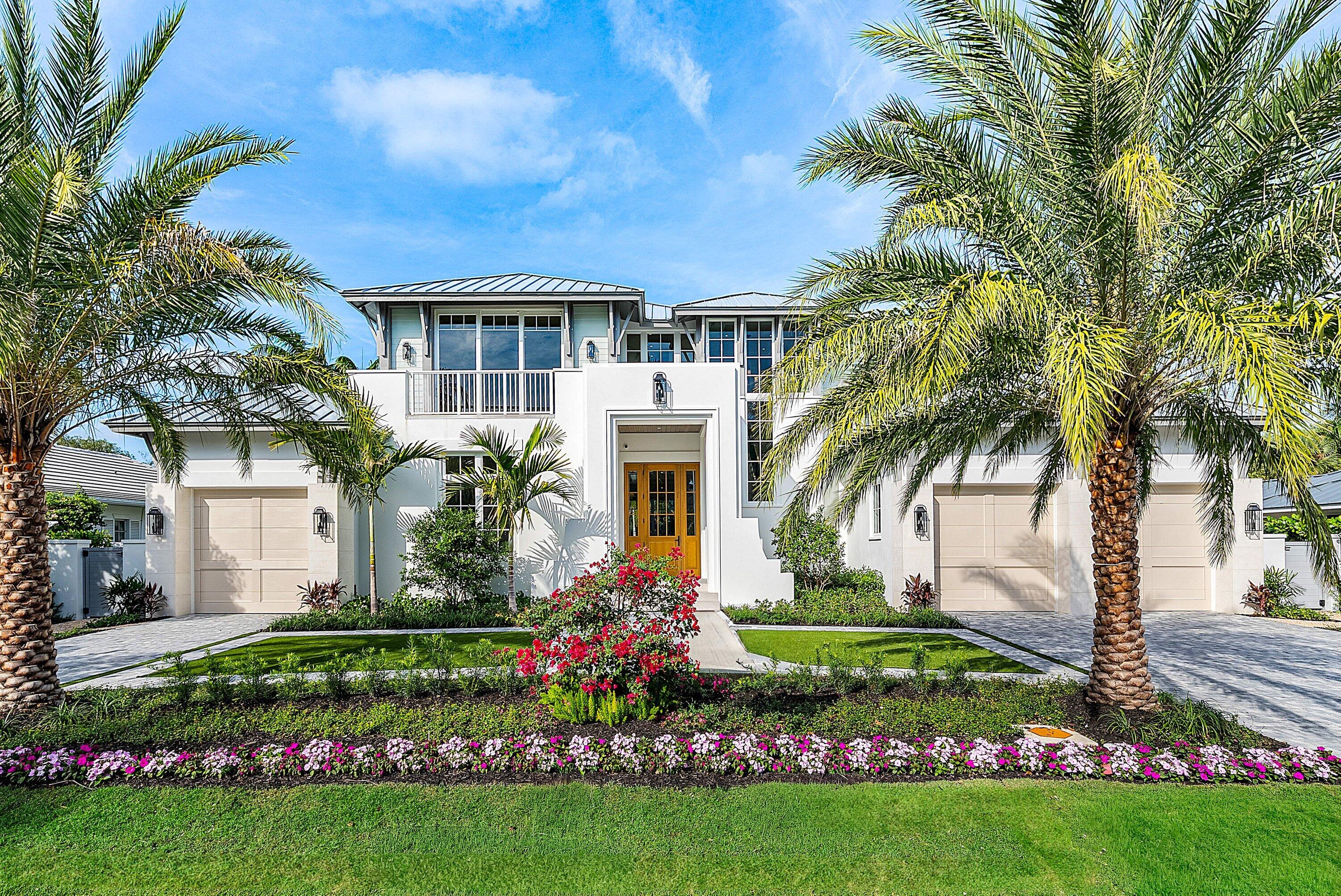 Modern white two-story home framed by palms, with a landscaped lawn and central walkway.