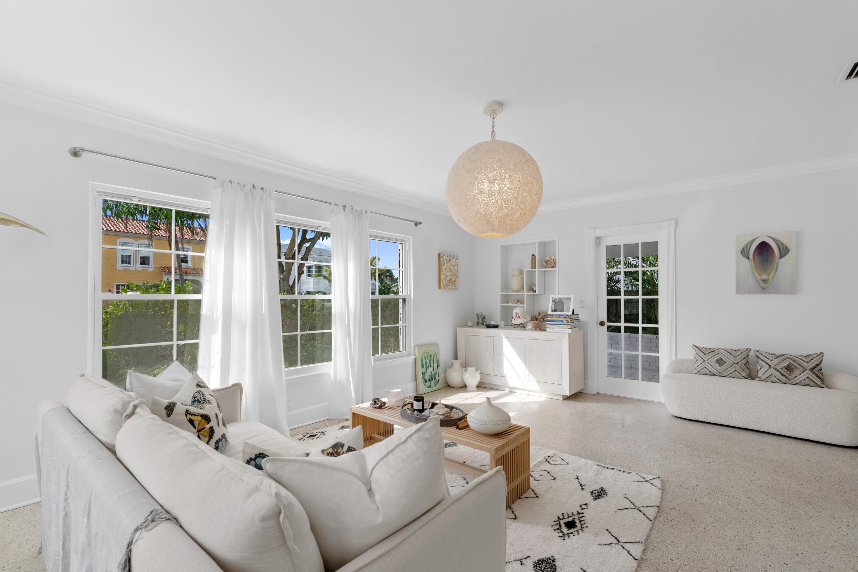 Bright living room with white sofas, tall curtained windows, and a sculptural pendant light.